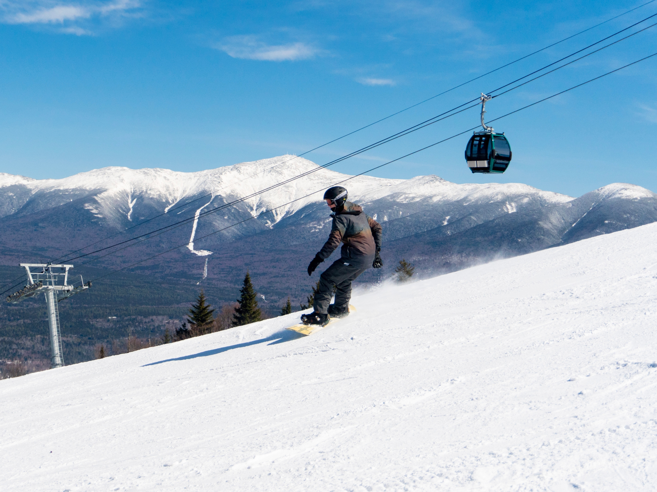 A snowboarder glides down the hill against a backdrop of snow-covered mountains at Bretton Woods.
