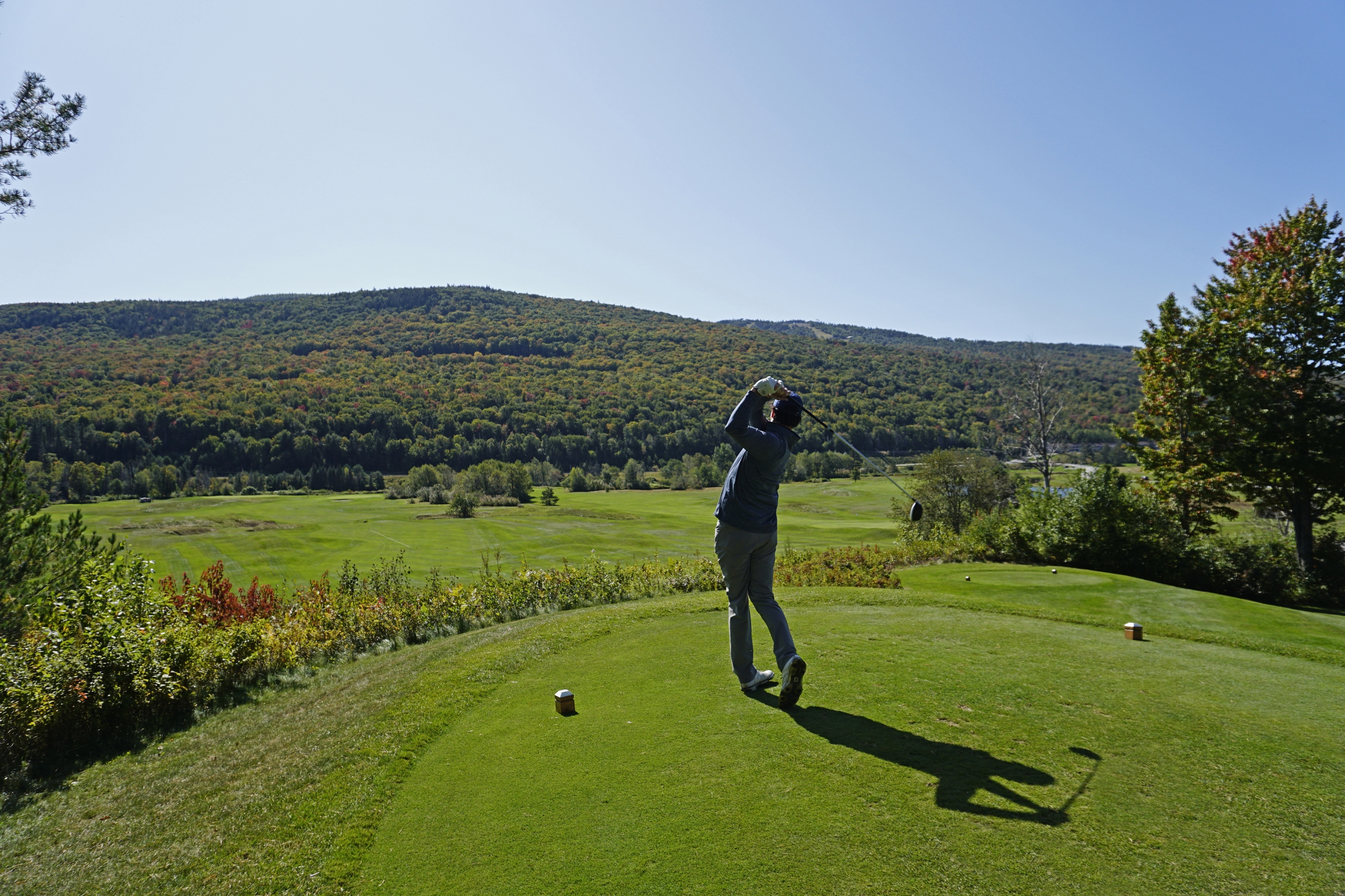 A golfer takes a swing on the golf course at Mount Washington Resort and Spa with a view of the lush green forest before him.