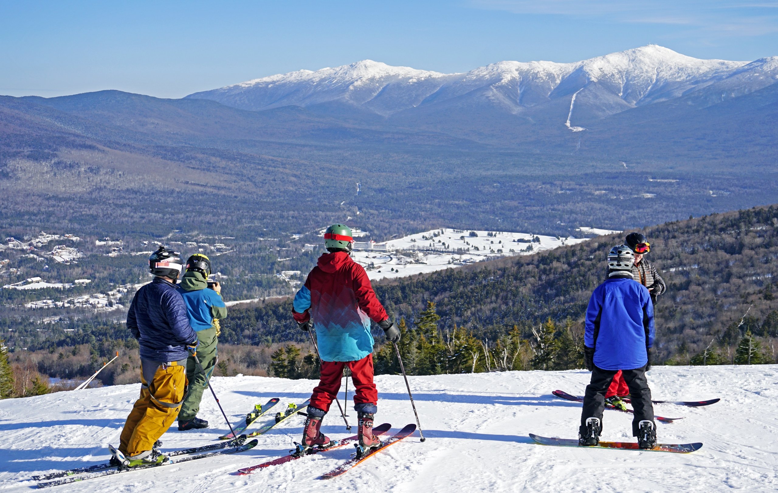 A group of skiers and snowboarders overlook a stunning view of lush forest and snow-covered mountains at Bretton Woods.