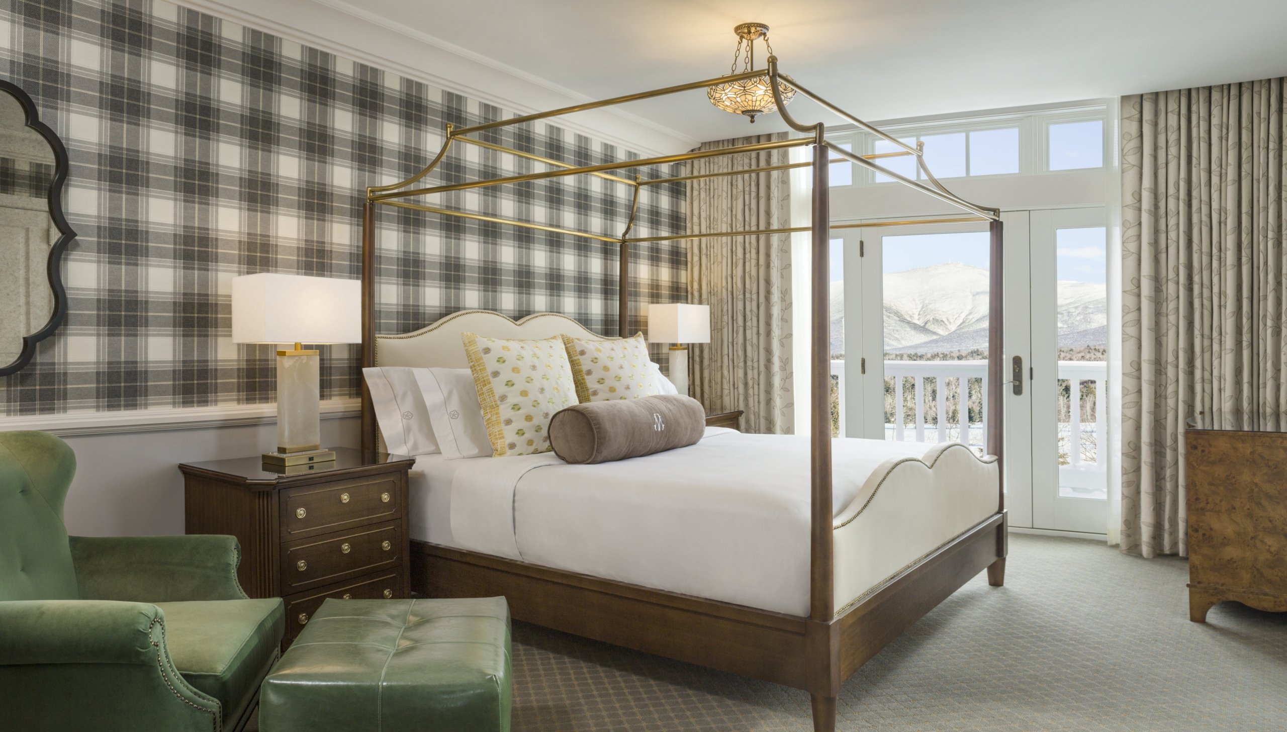 The Executive Presidential Suite at Mount Washington Resort and Spa features a four-poster bed, warm wooden furniture, and a large window with a scenic view of mountains in the distance.