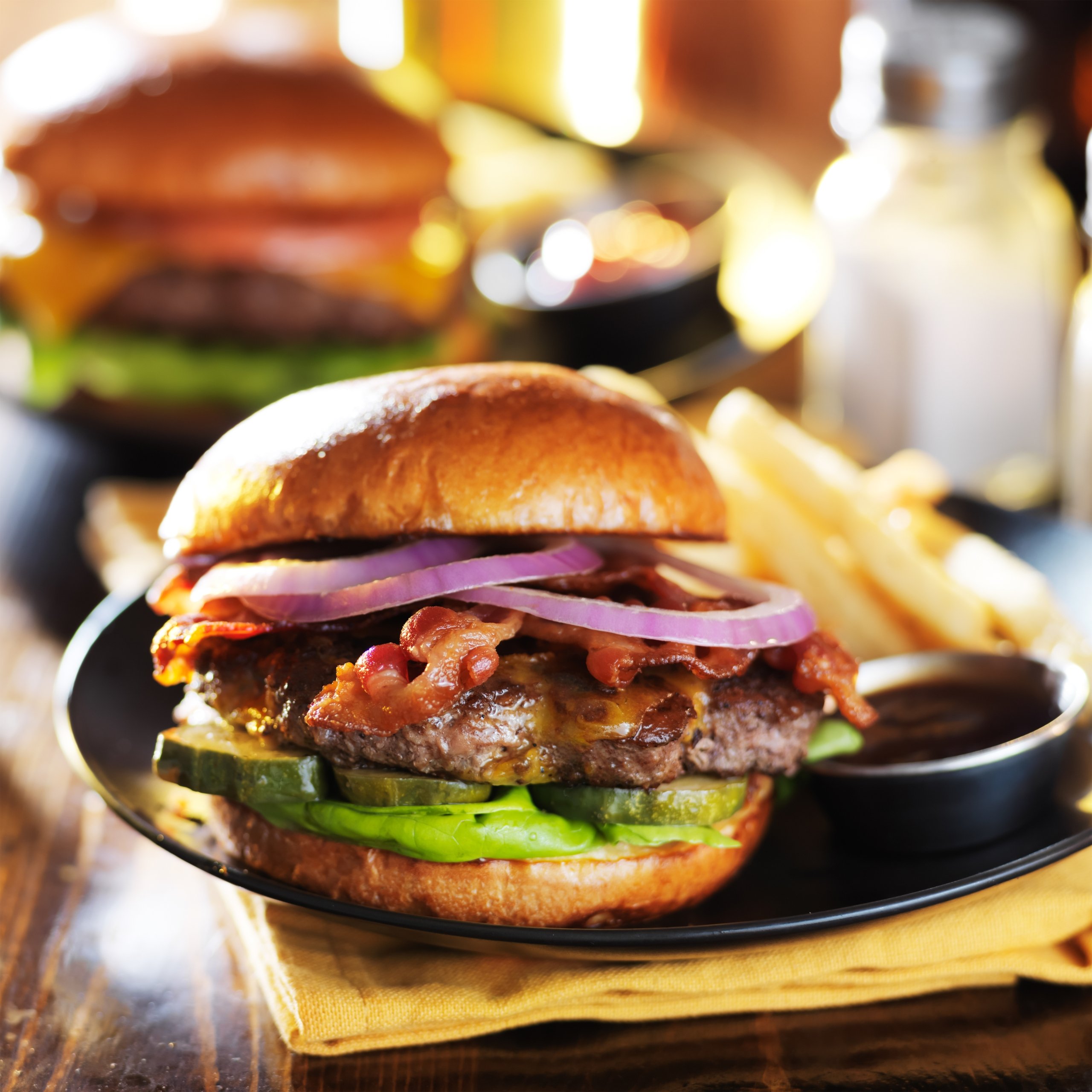Close-up of a cheeseburger with lettuce, tomato, and onion served with fries and dipping sauce.