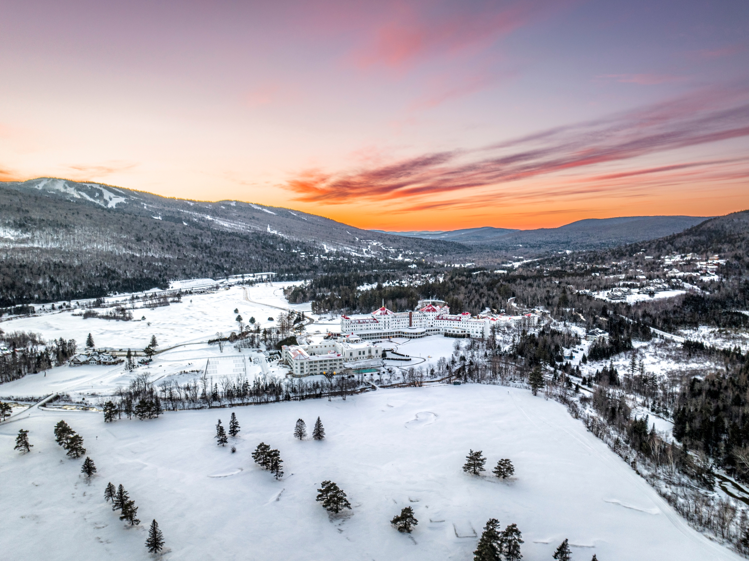 Mount Washington Resort and Spa sits at the base of snowy mountains glowing under a colorful sunset.