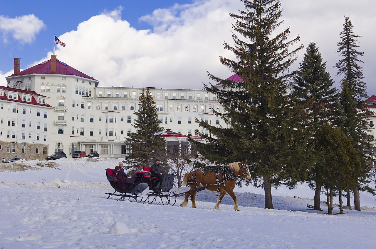 A horse pulls a family on a sleigh on the snow-covered lawn in front of Mount Washington Resort and Spa.