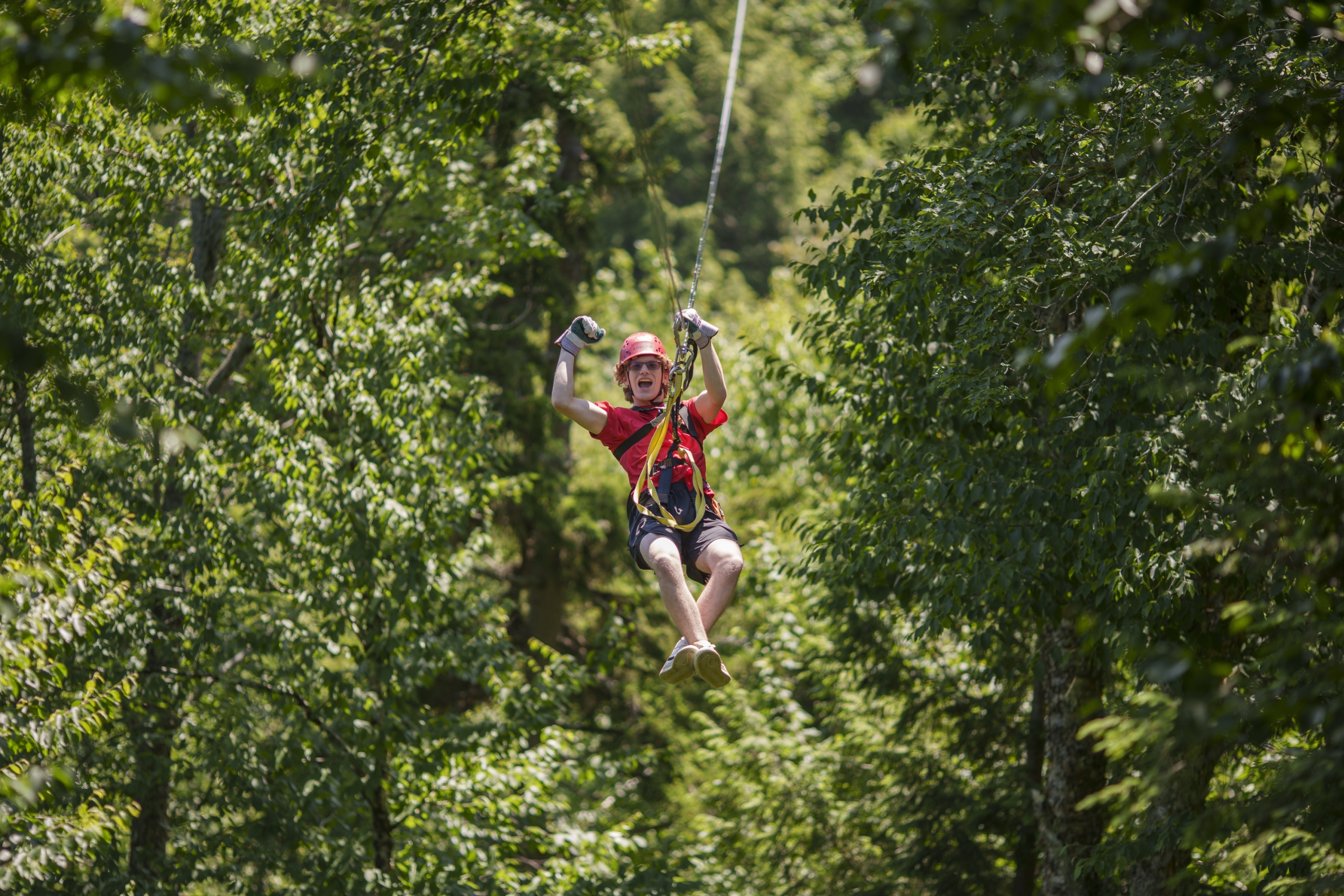 A man pumps his fist as he races across a zip-line.