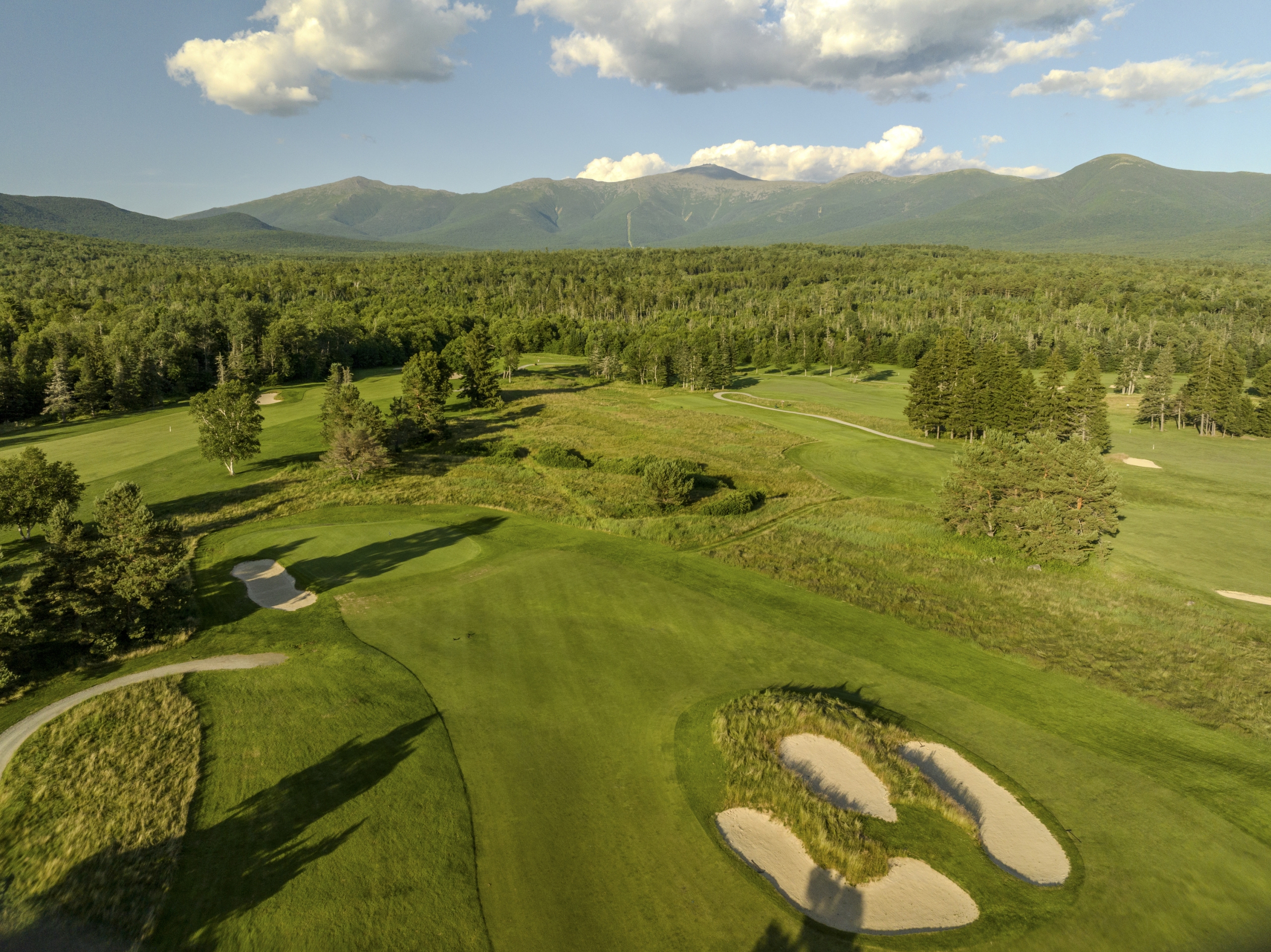 The lush green golf course at Mount Washington Resort and Spa stretches out beneath a clear blue sky, surrounded by forest and rolling hills.