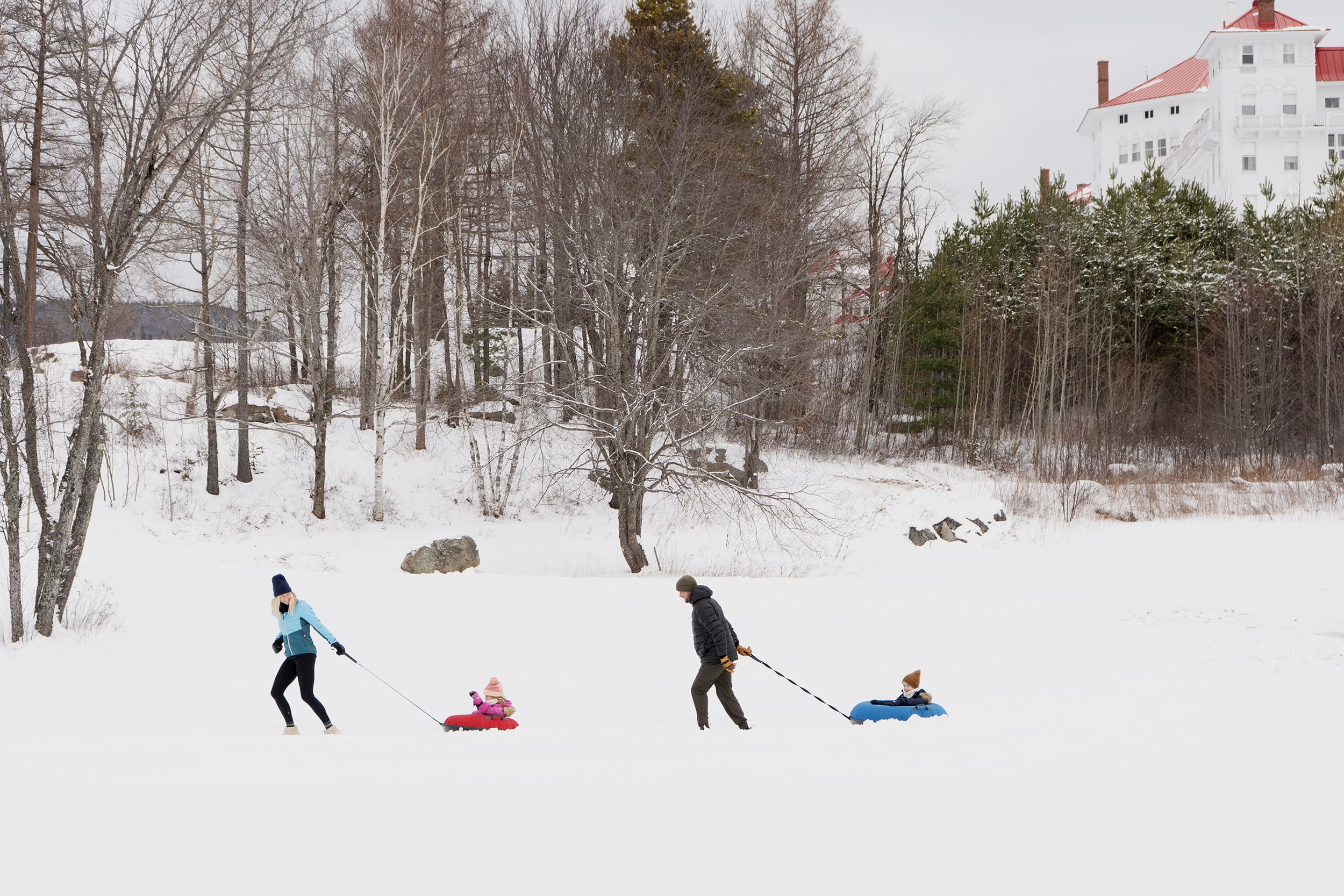 Family of four pulling each other on tubes at Omni Mount Washington Resort & Spa tubing hill in winter.