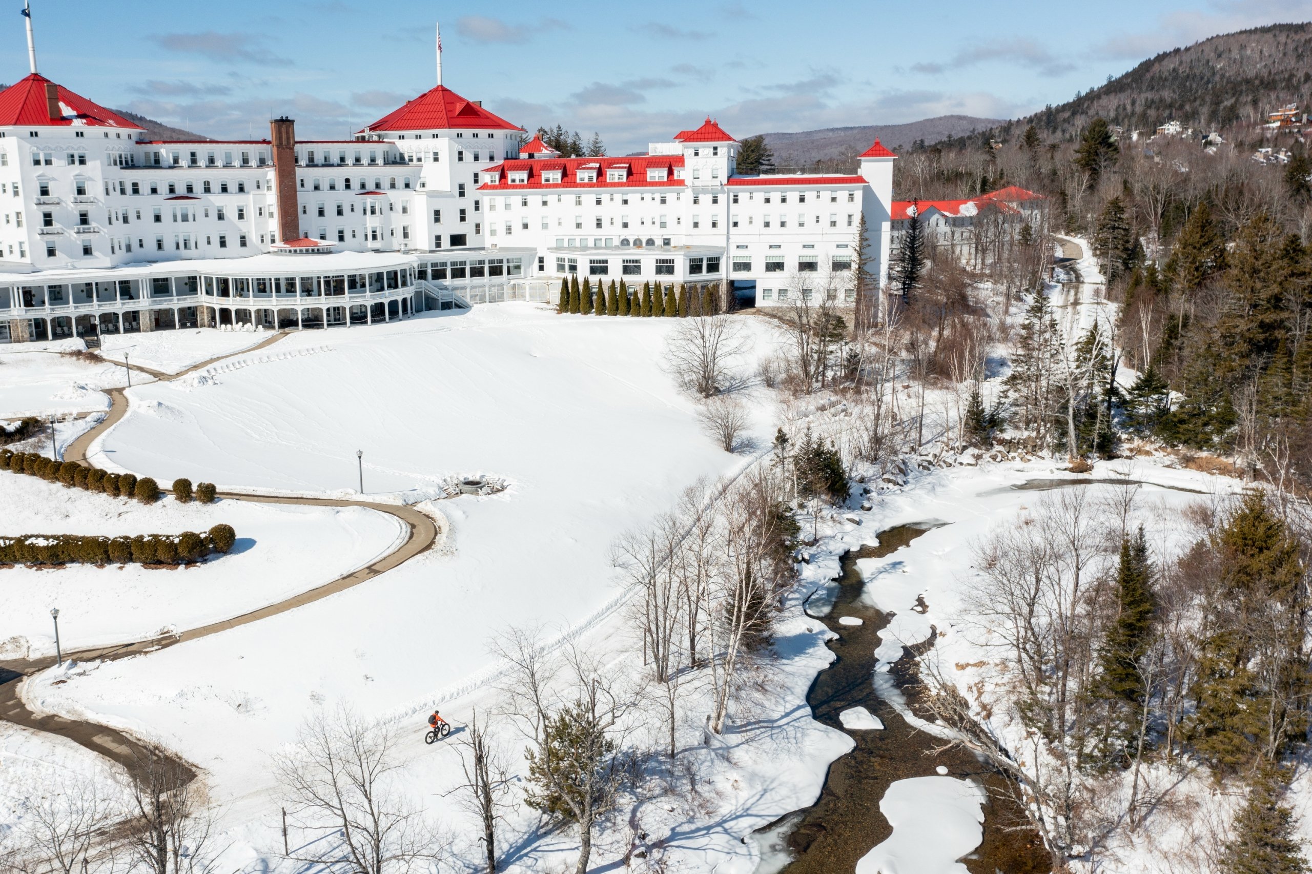 The white exterior and red roof of Mount Washington Resort and Spa glistens in the snow on a sunny day.