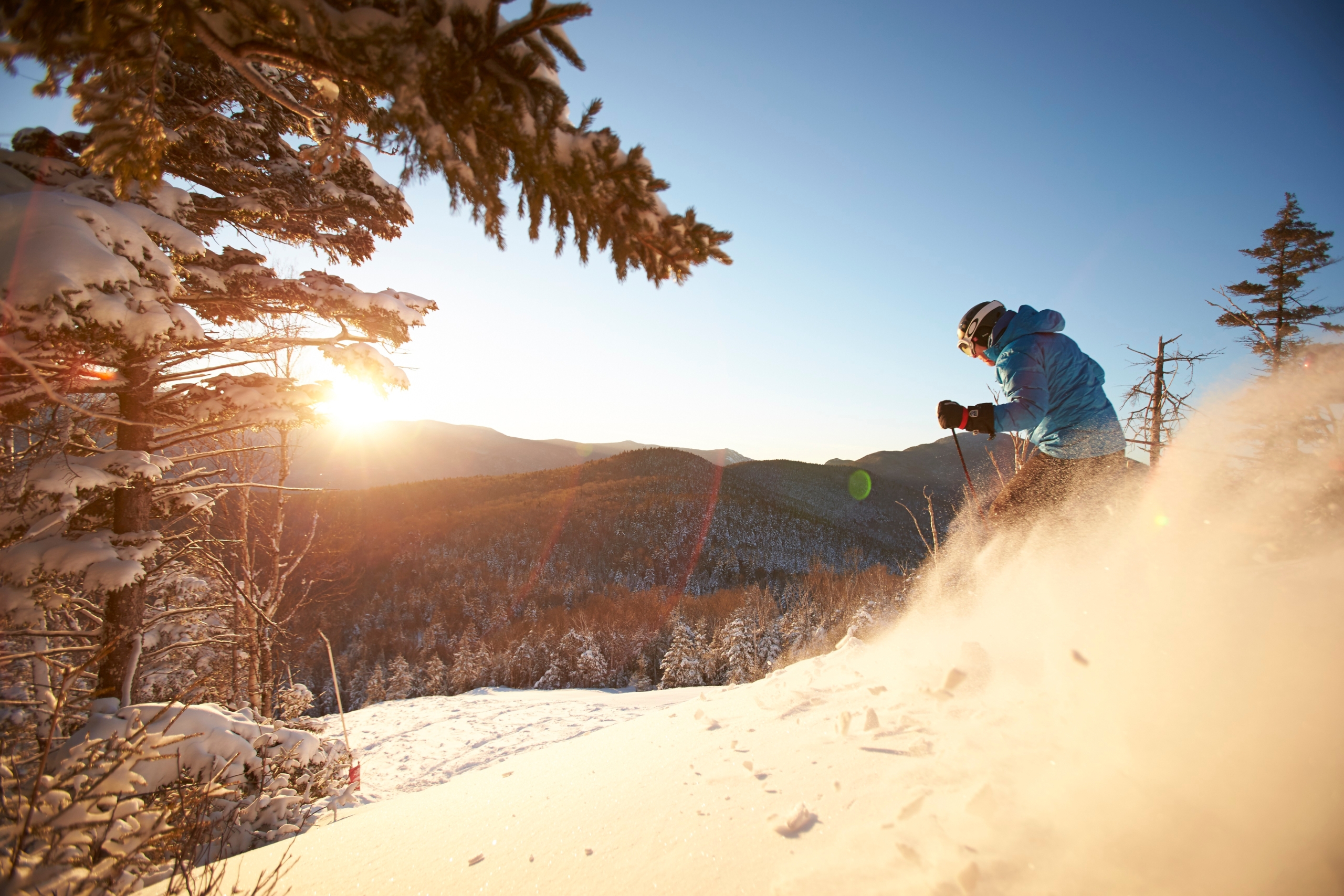A skier pivots in the snow, spraying powder in the air, while skiing down the hill on a sunny day at Bretton Woods.