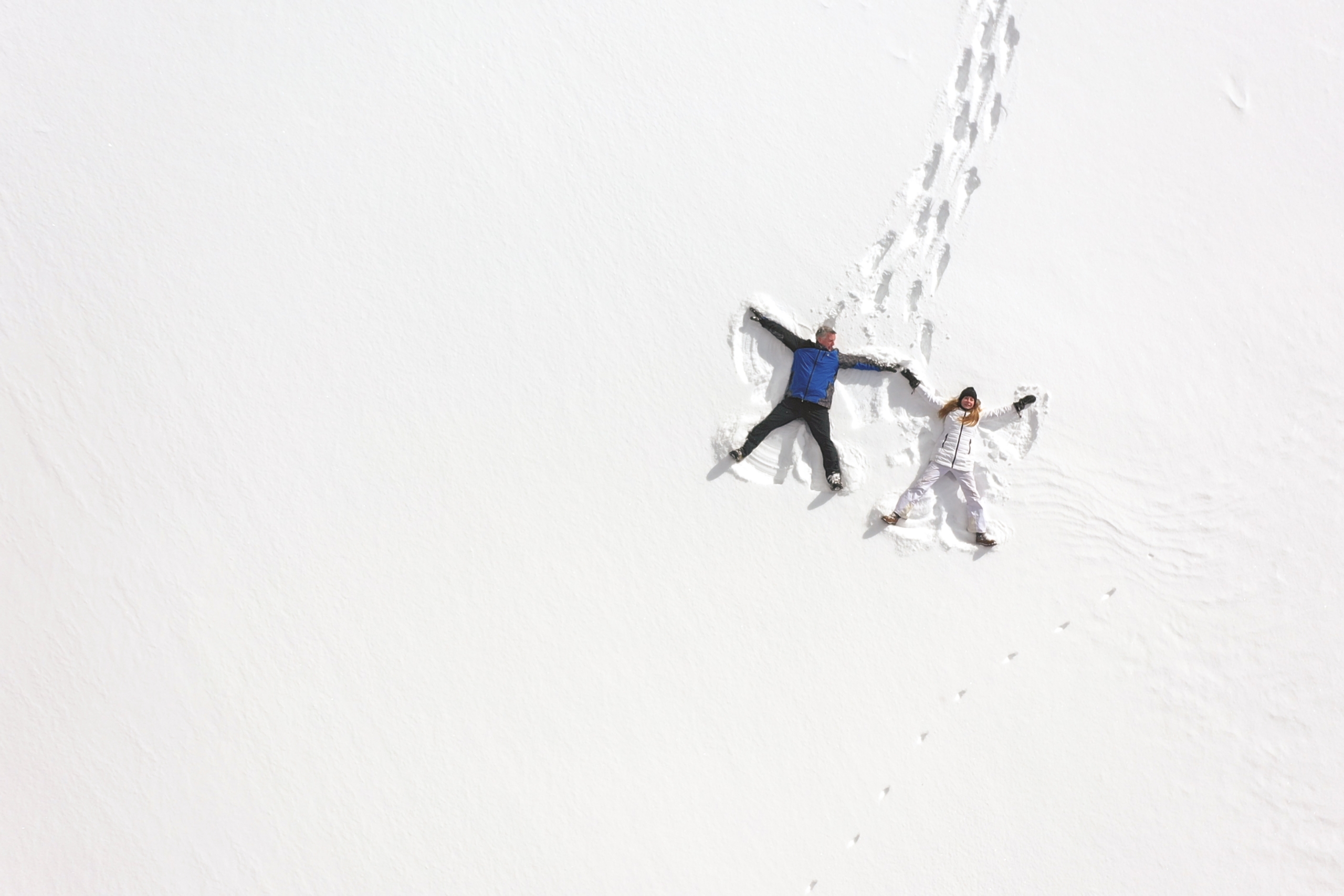 A man and woman lay in the crisp white snow making snow angels together at Mount Washington Resort and Spa.