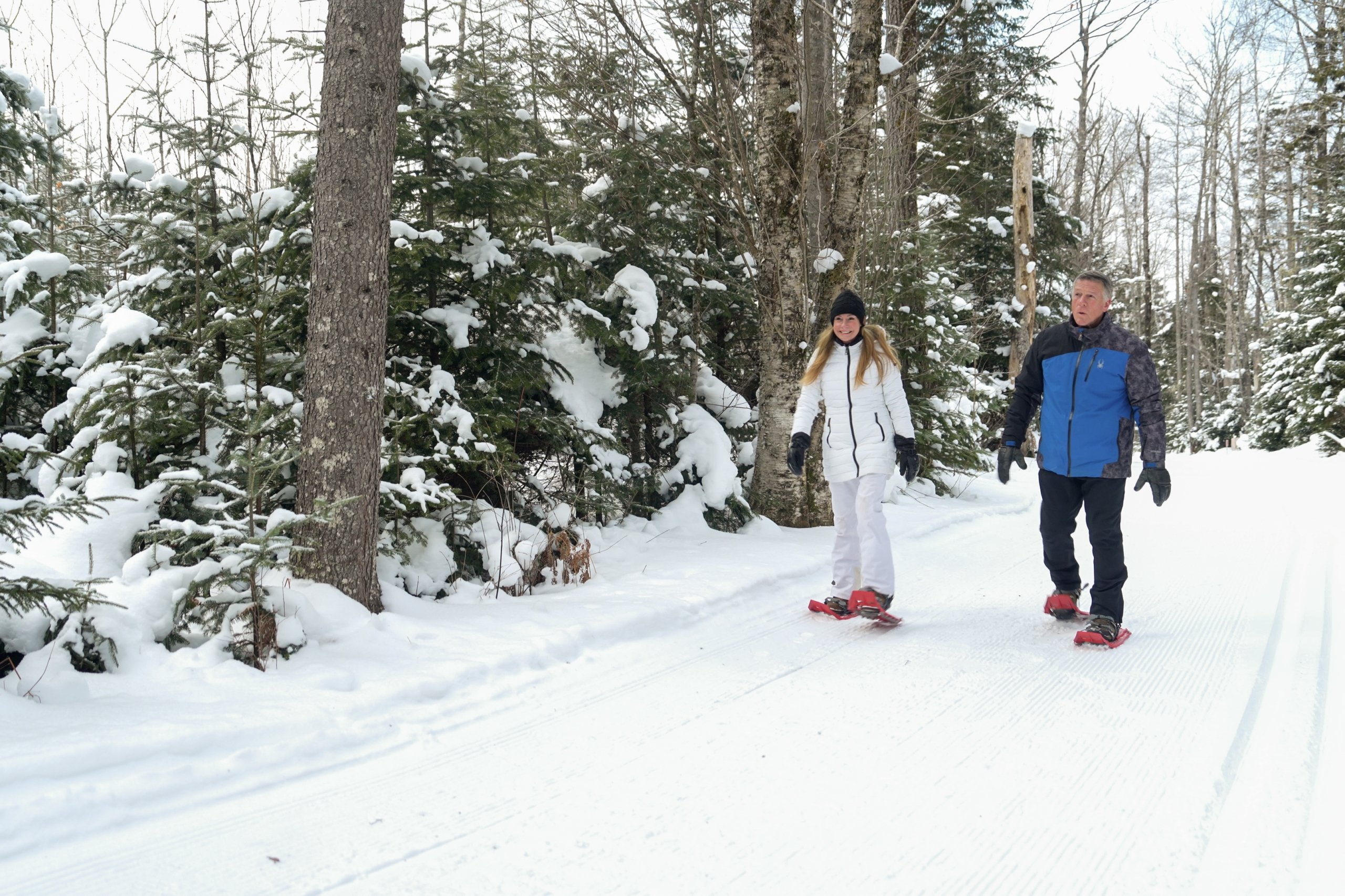A man and woman snowshoe on a trail at Mount Washington Resort and Spa.