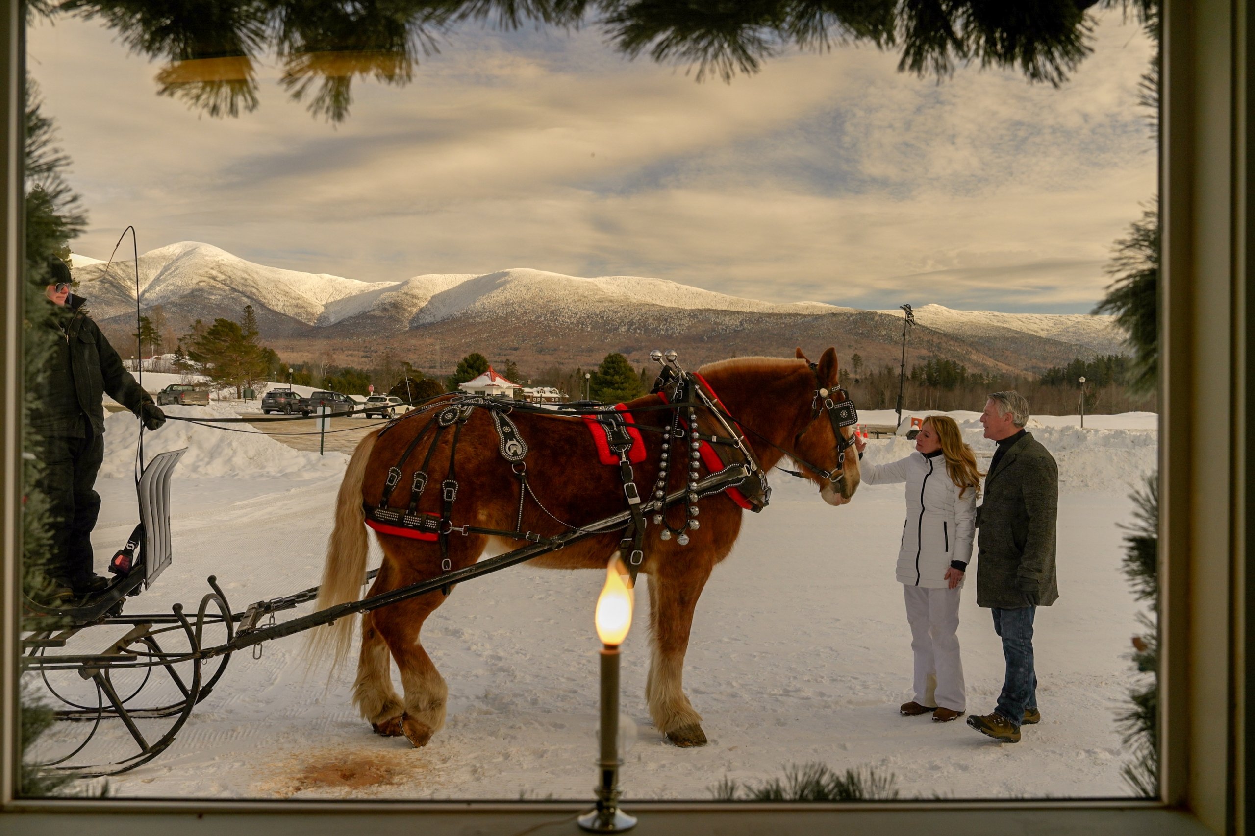 A man and woman greet a horse pulling a sleigh in the snow at Mount Washington Resort and Spa.