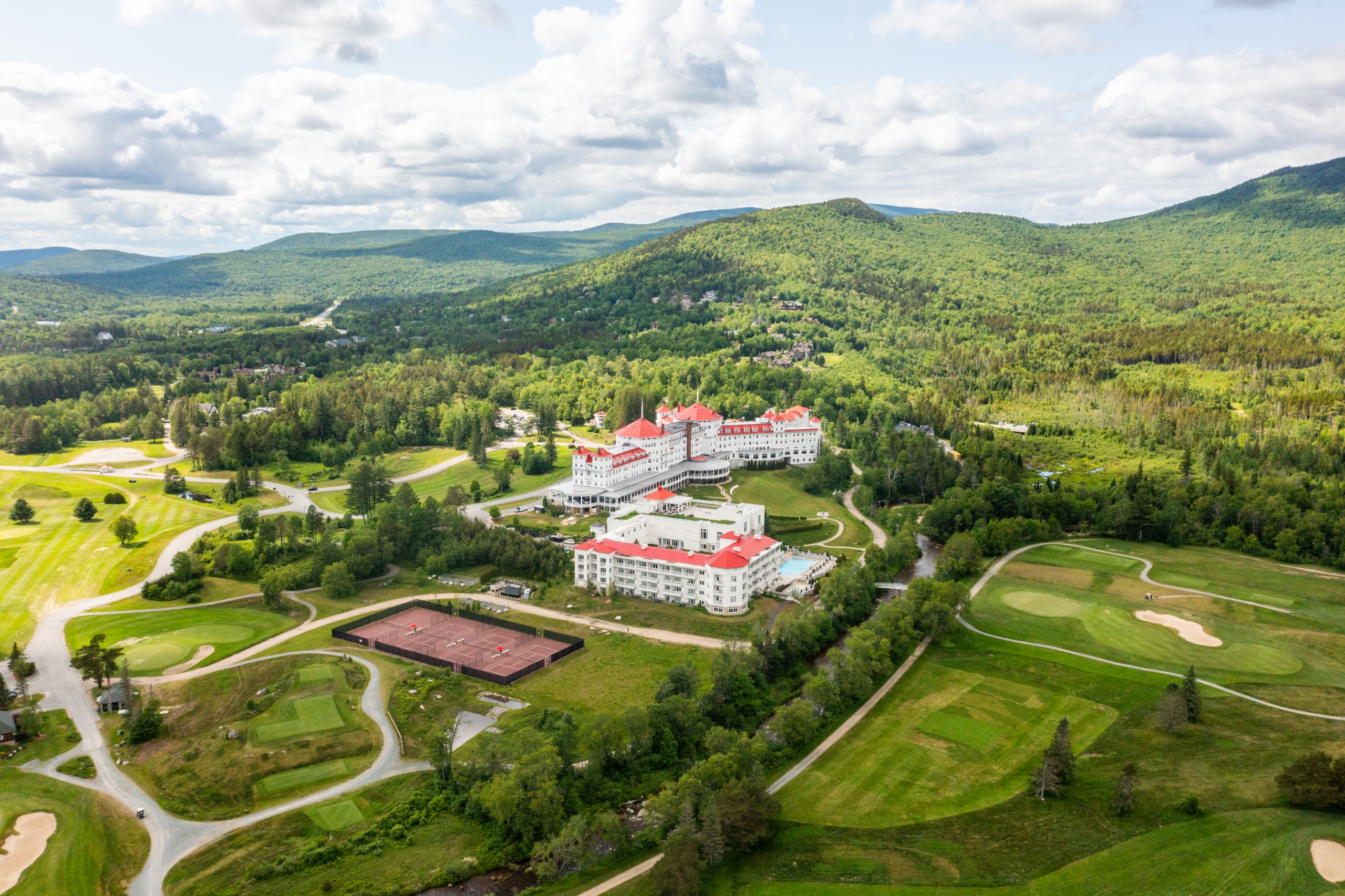 The white exterior and red roofs of Mount Washington Resort and Spa pop against a backdrop of a lush green forest and golf course.