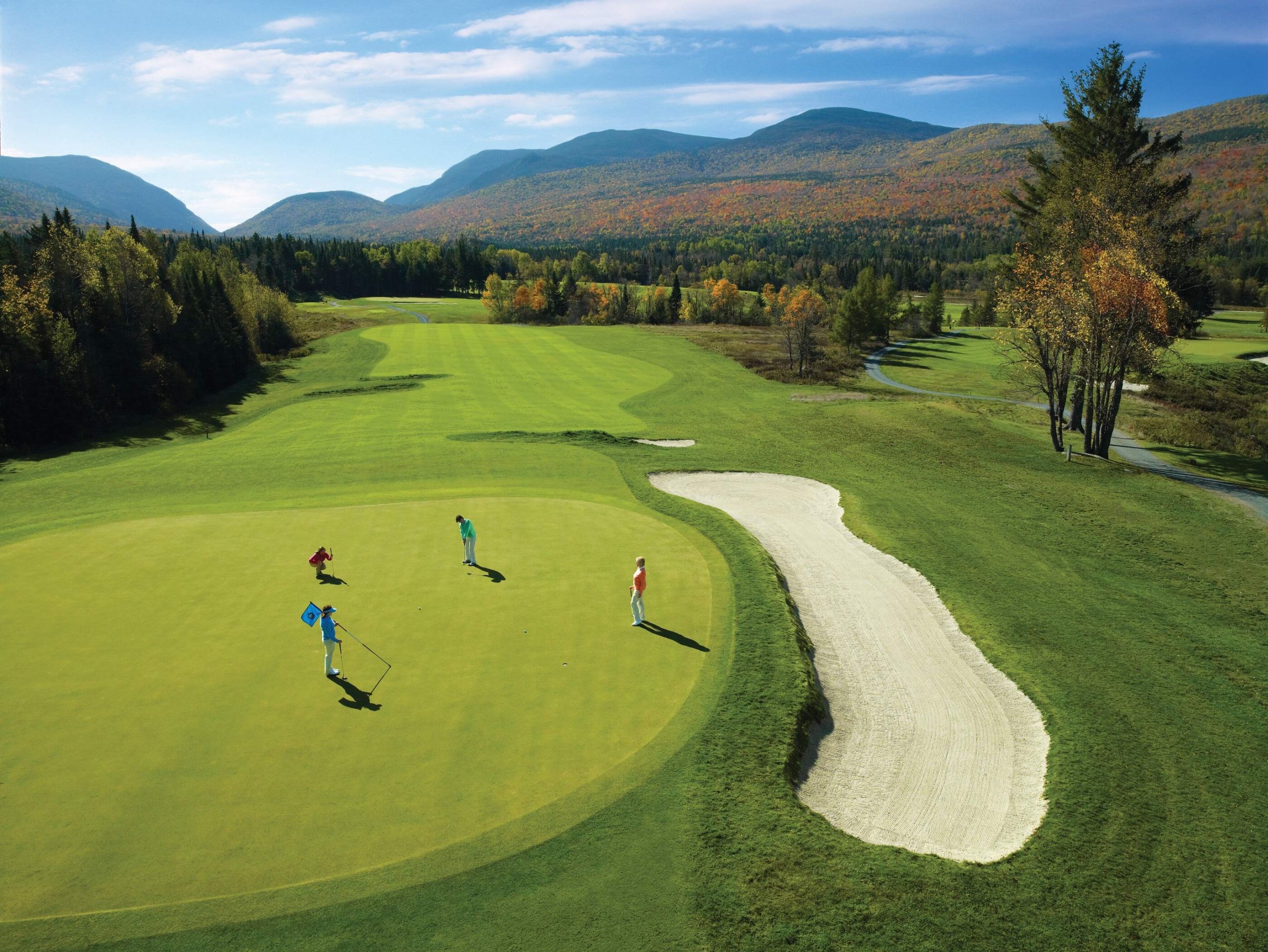 A group of golfers on the putting green with a stunning view of the forest and mountains at Mount Washington Resort and Spa.