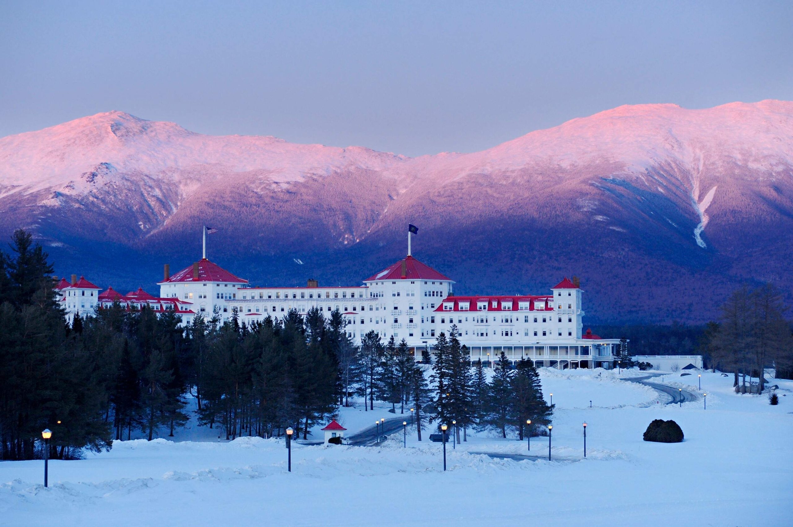 Mount Washington Resort and Spa sits at the base of snowy mountains glowing under a colorful sunset.