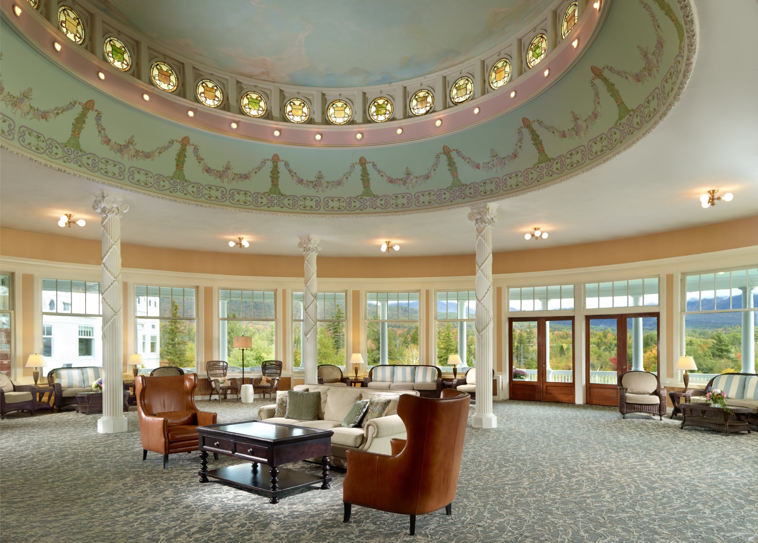 Elegant conservatory with large windows, classic columns, and comfortable seating overlooking a scenic mountain view at Mount Washington Resort and Spa.