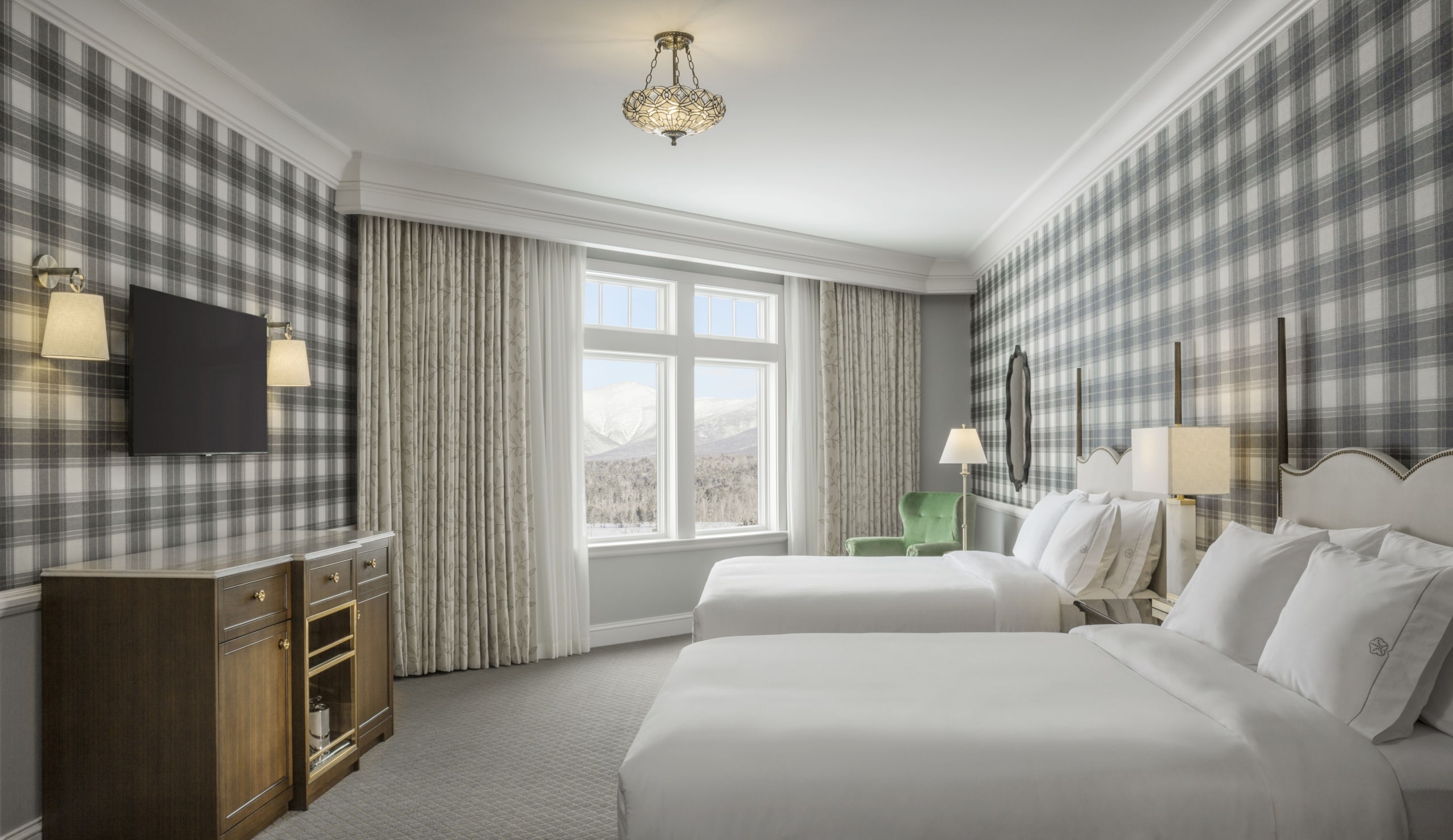 Two hotel beds face a large window with a scenic view of snowy mountains in the Presidential room at Mount Washington Resort and Spa.