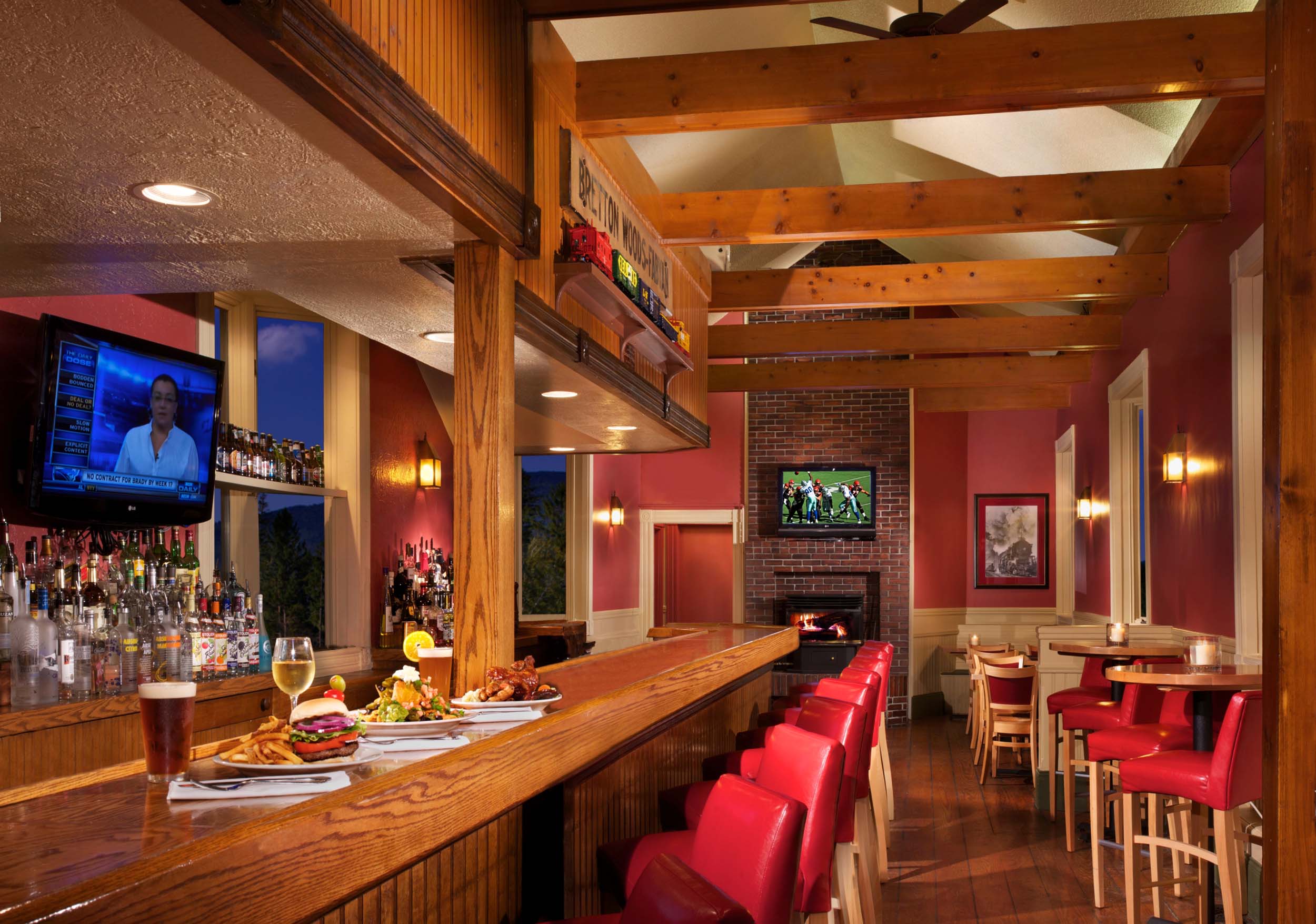 Cozy bar with red leather chairs, wooden beams, and TVs above a warm fireplace at Fabyan's Station Restaurant and Lounge.