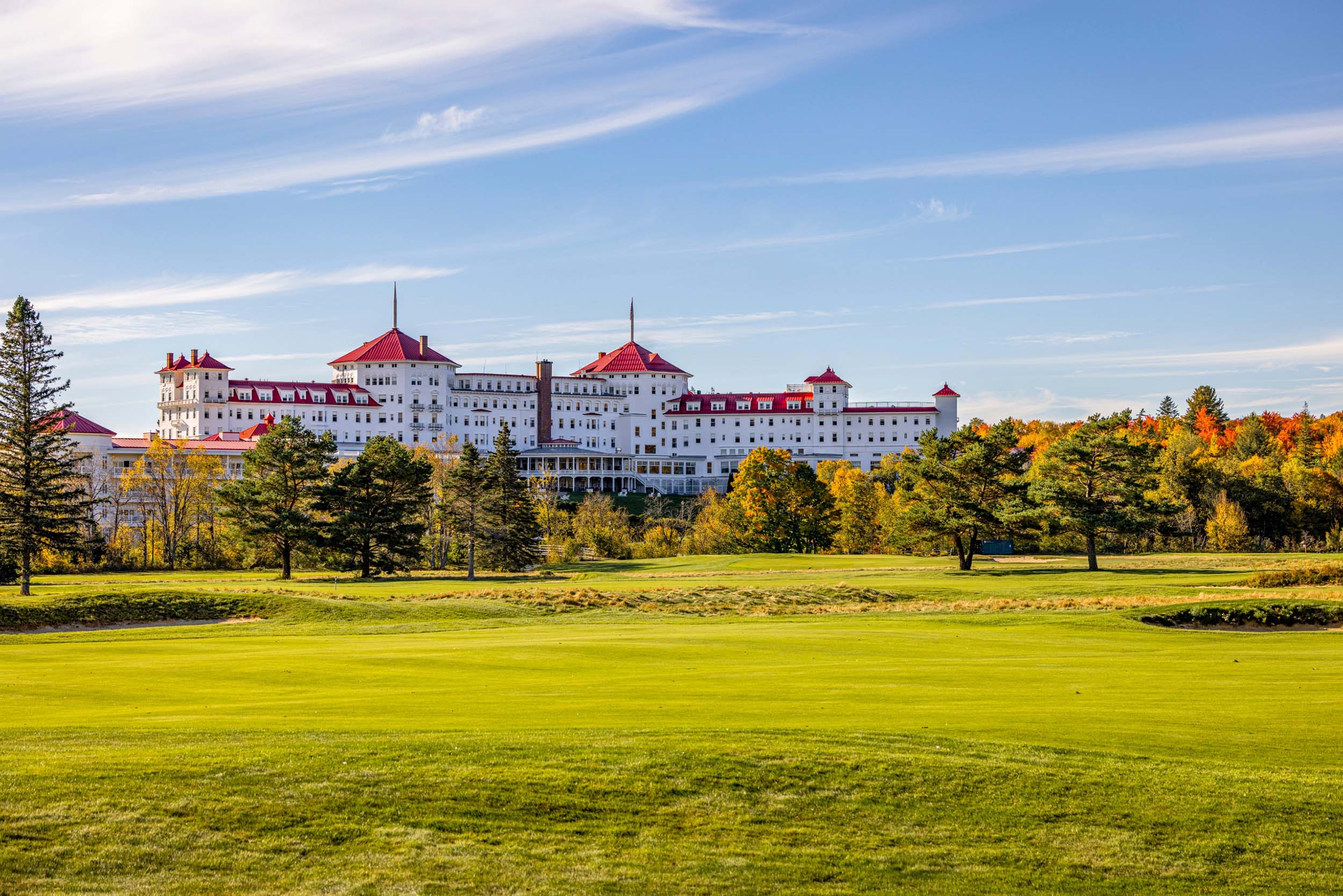 The white exterior and red roof of Mount Washington Resort and Spa pops amongst the forest of trees in vibrant fall colours and lush green golf course.