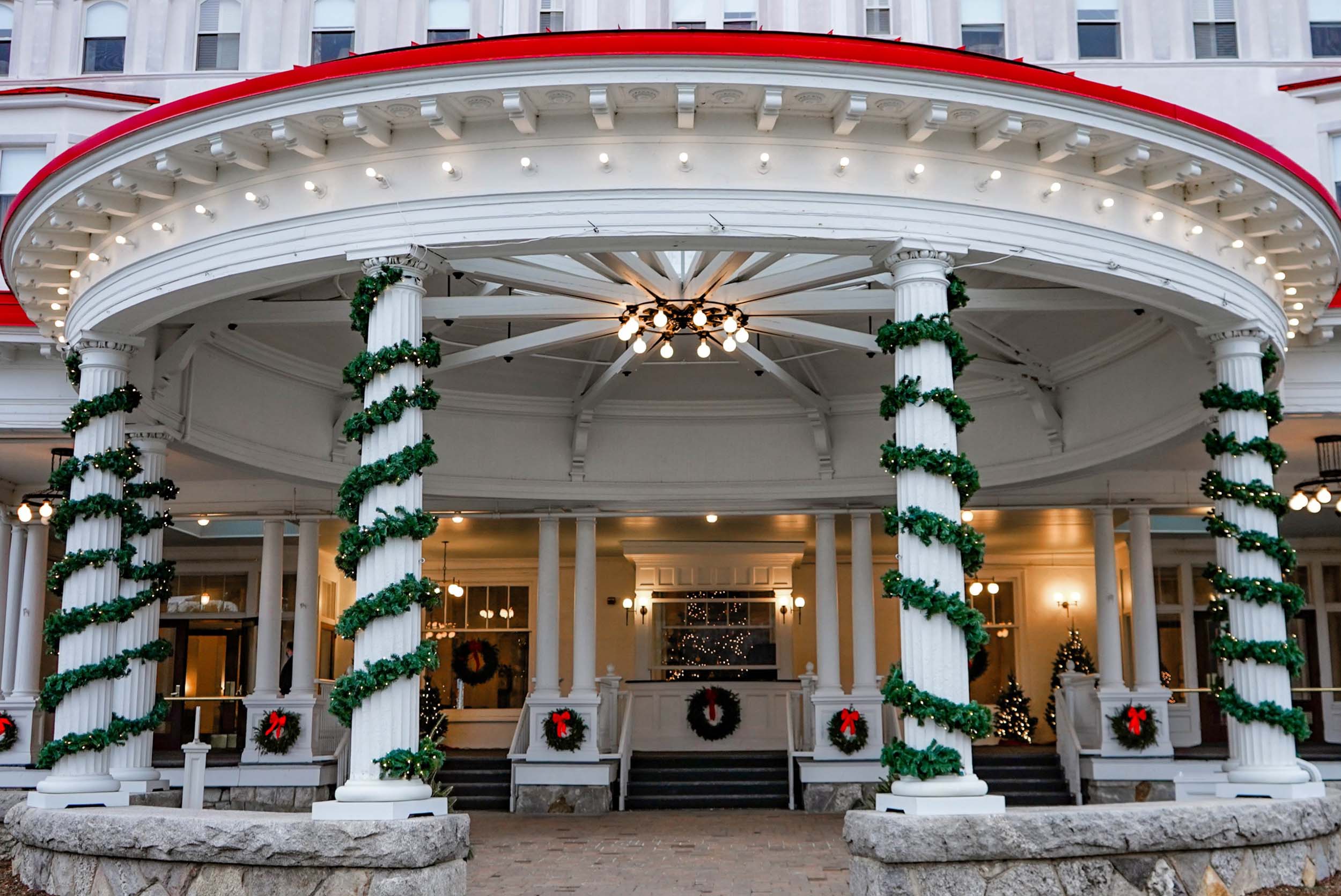The entrance of a Mount Washington Resort and Spa decorated with green garlands, wreaths, and festive lights around white columns.