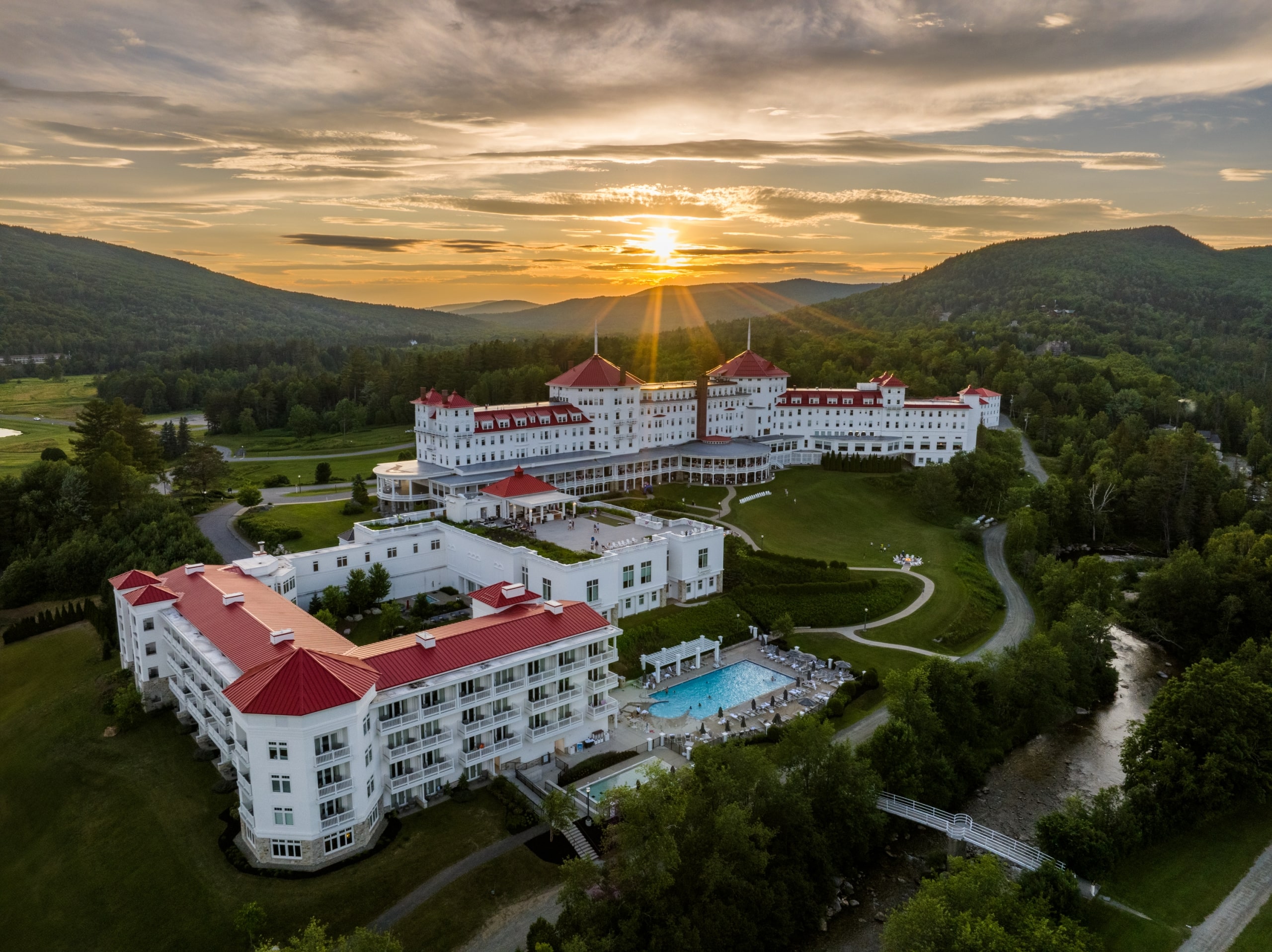 Aerial view of Mount Washington Resort and Spa nestled in a lush green valley, surrounded by forested mountains at sunset.