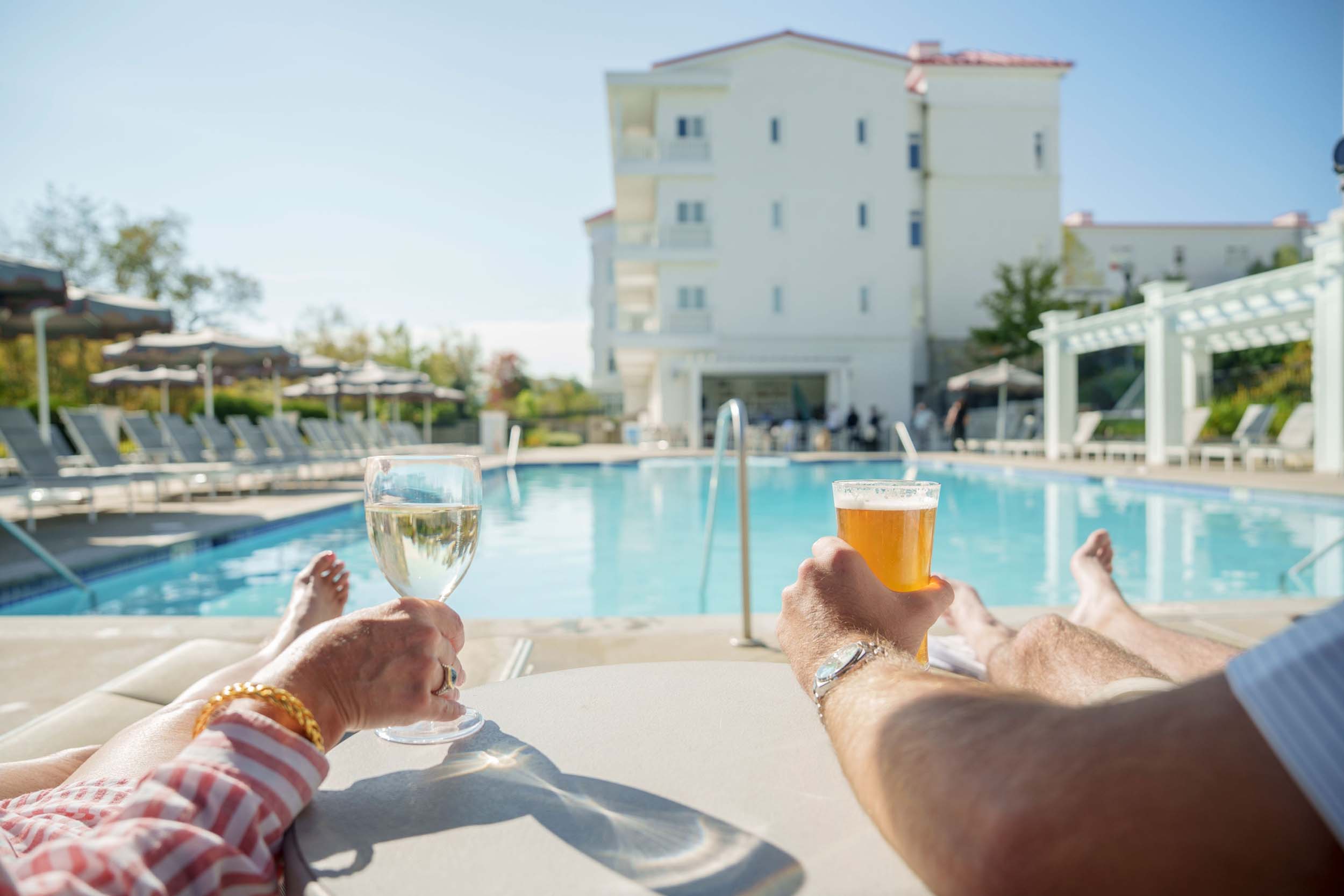 Two people relax on lounge chairs, each holding a drink, beside a sunny outdoor pool at Mount Washington Resort and Spa.