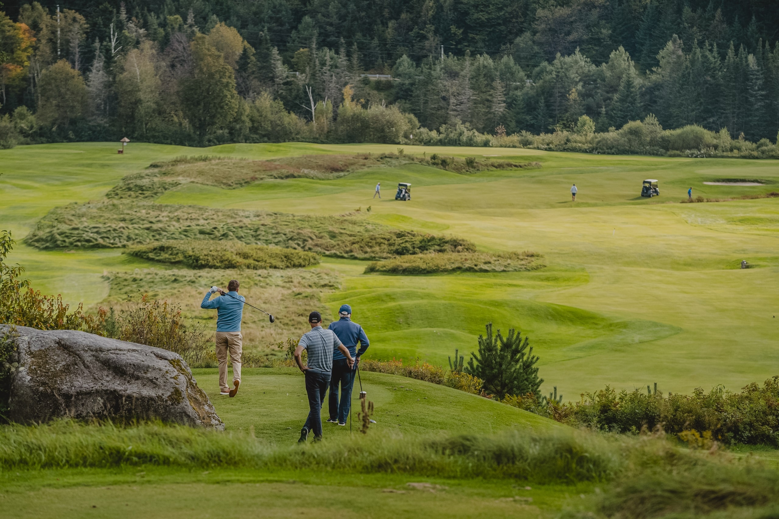 A group of golfers watch on as their teammate takes a swing on the course at Mount Washington Resort and Spa.