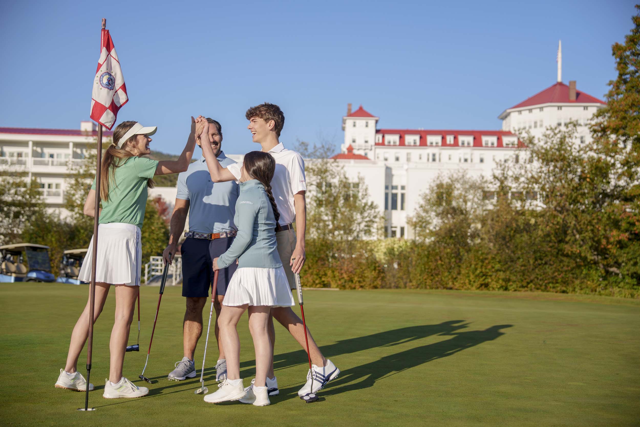 A family joyfully high-fives on the golf course at Mount Washington Resort and Spa.