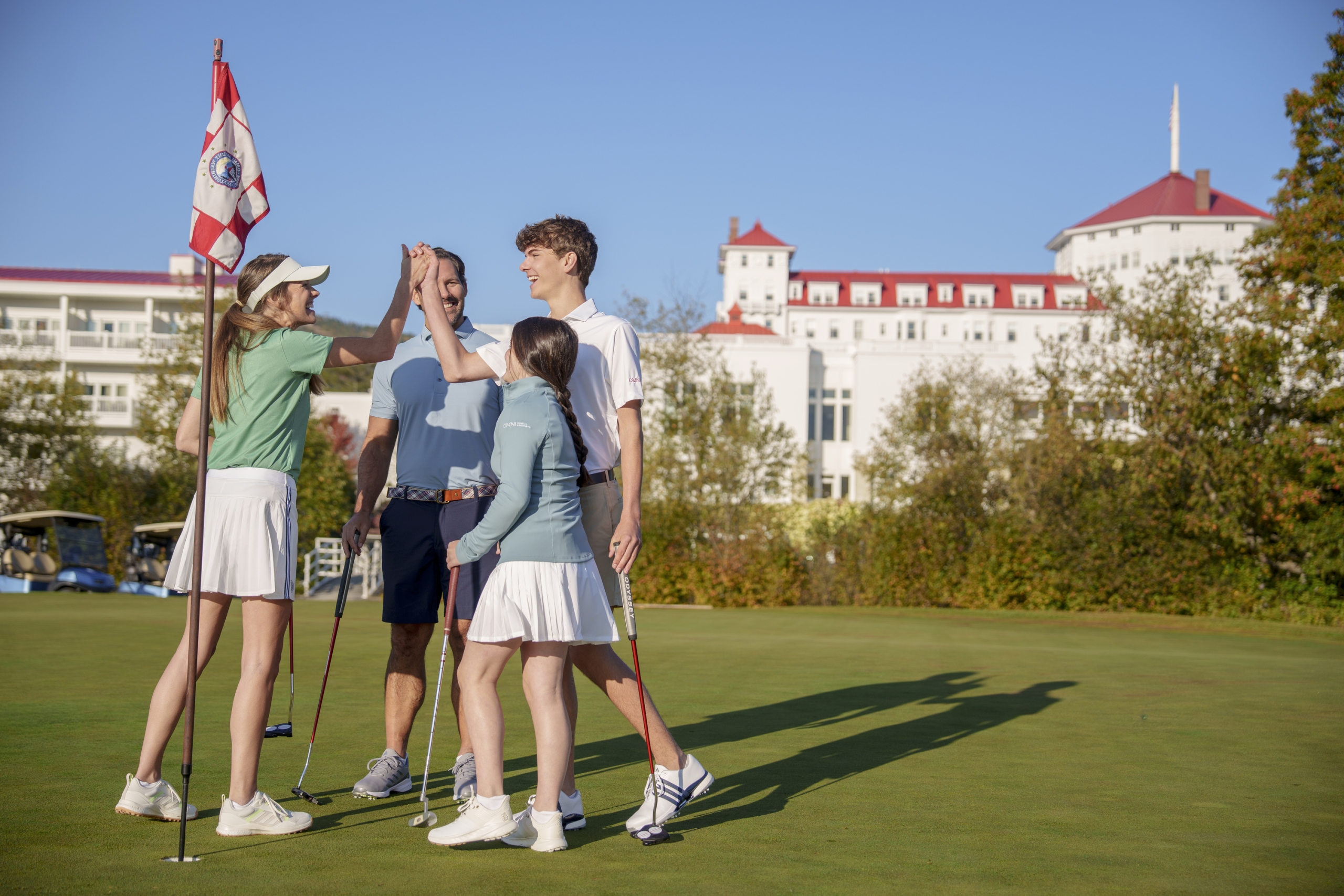 A family joyfully high-fives on the golf course at Mount Washington Resort and Spa.