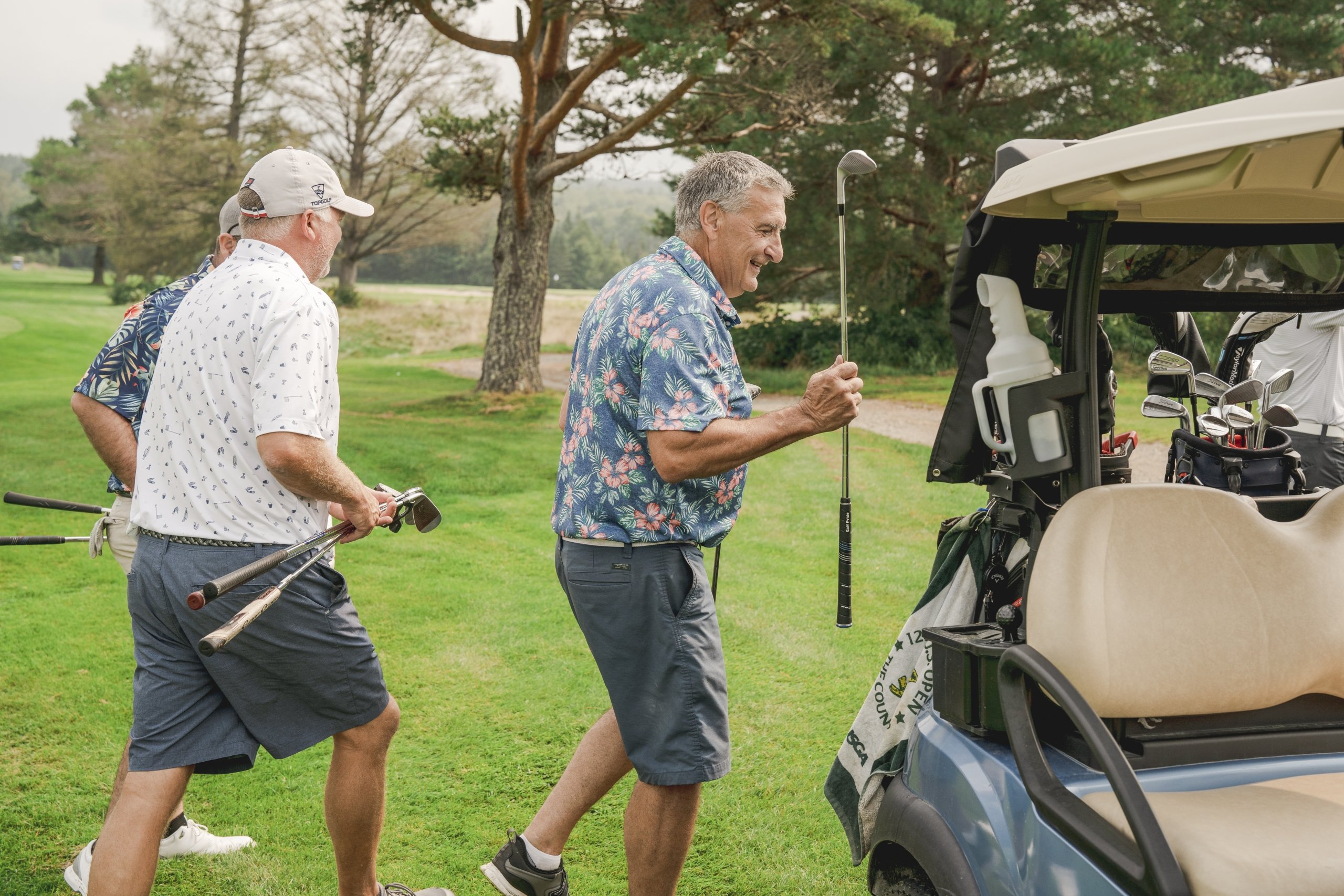 Three men walk toward a golf cart while carrying their clubs on a sunny golf course at Mount Washington Resort and Spa.