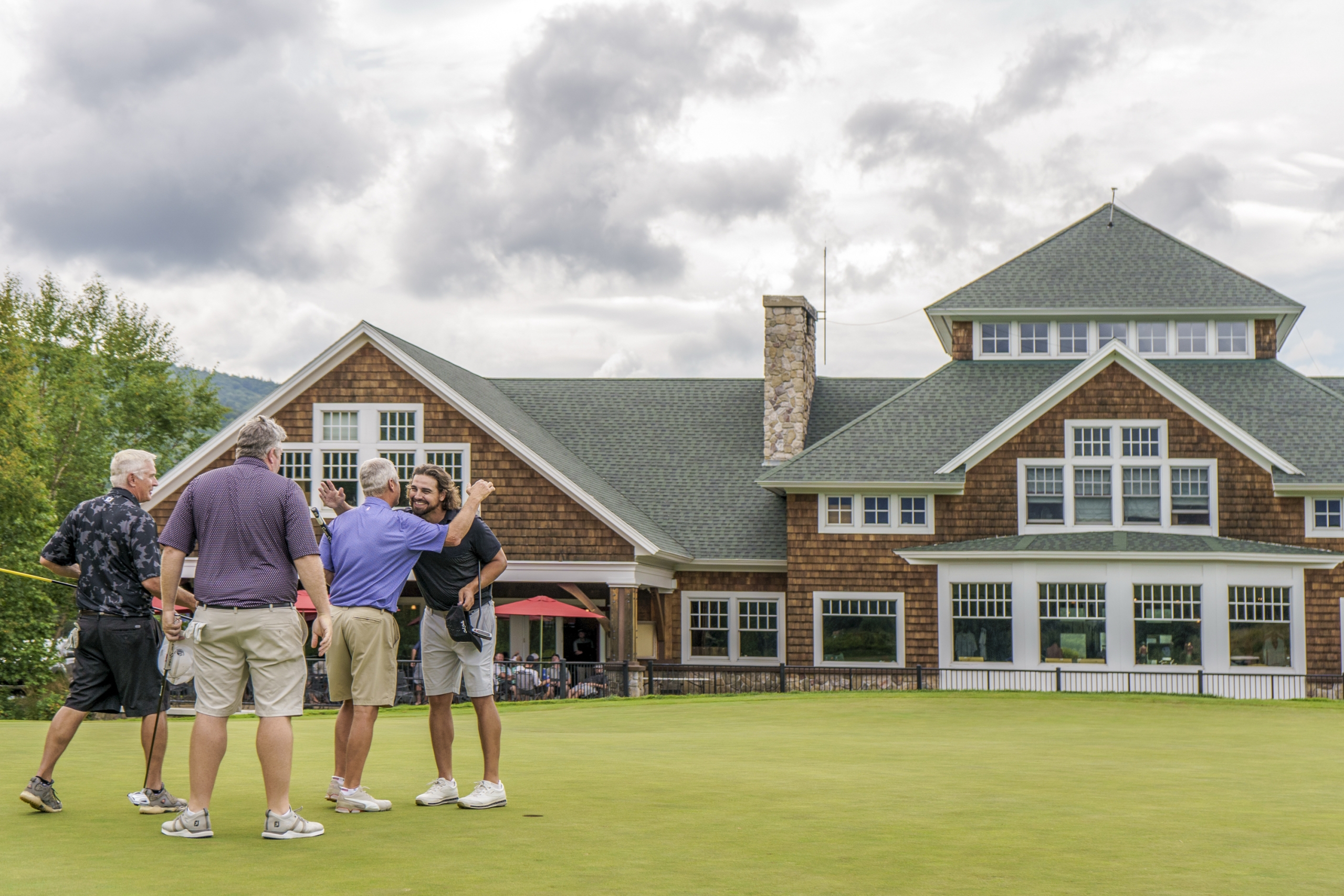 A group of male golfers warmly greet each other on the green in front of the club house at Mount Washington Resort and Spa.