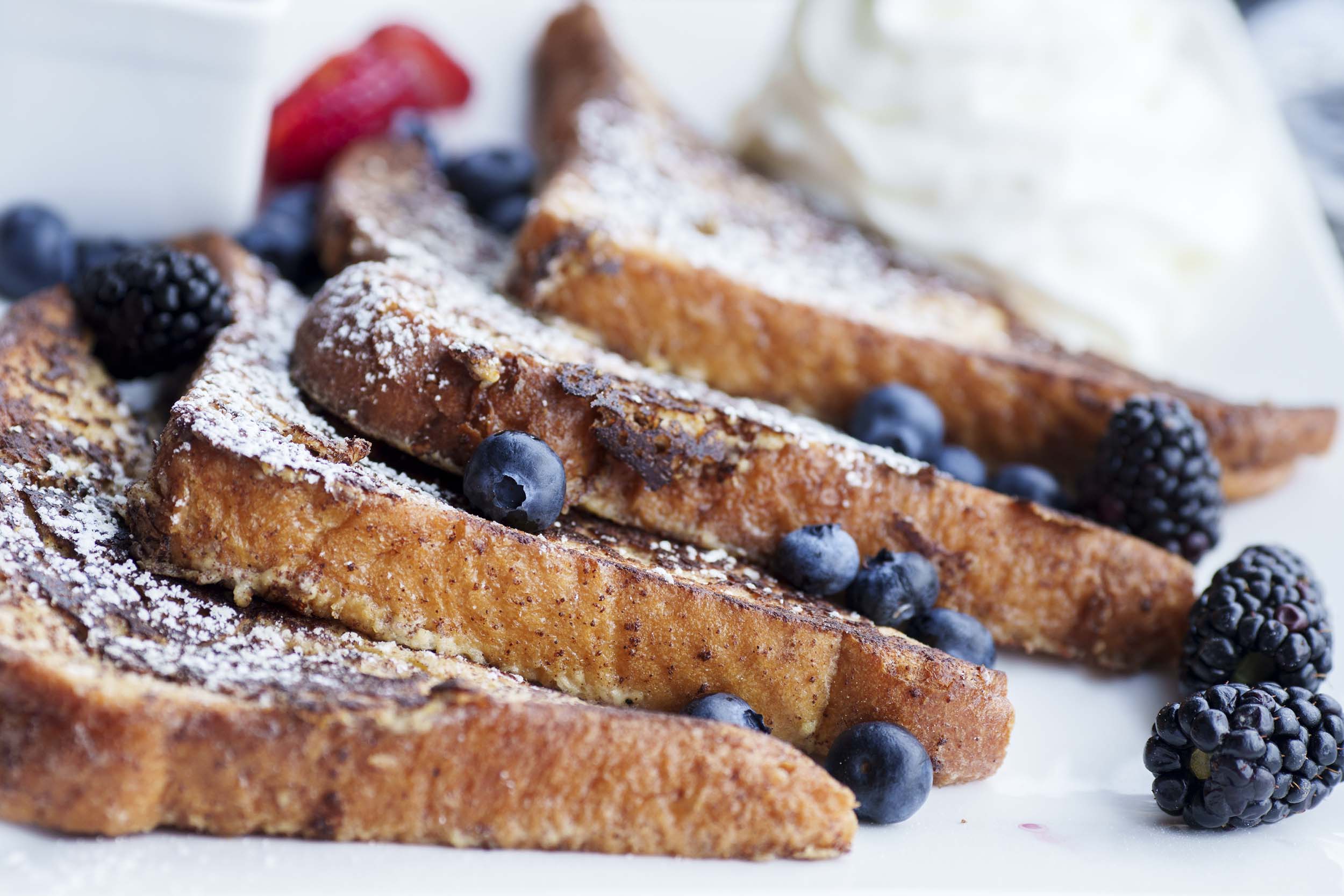 French toast laid out with berries, icing sugar and whipped cream.