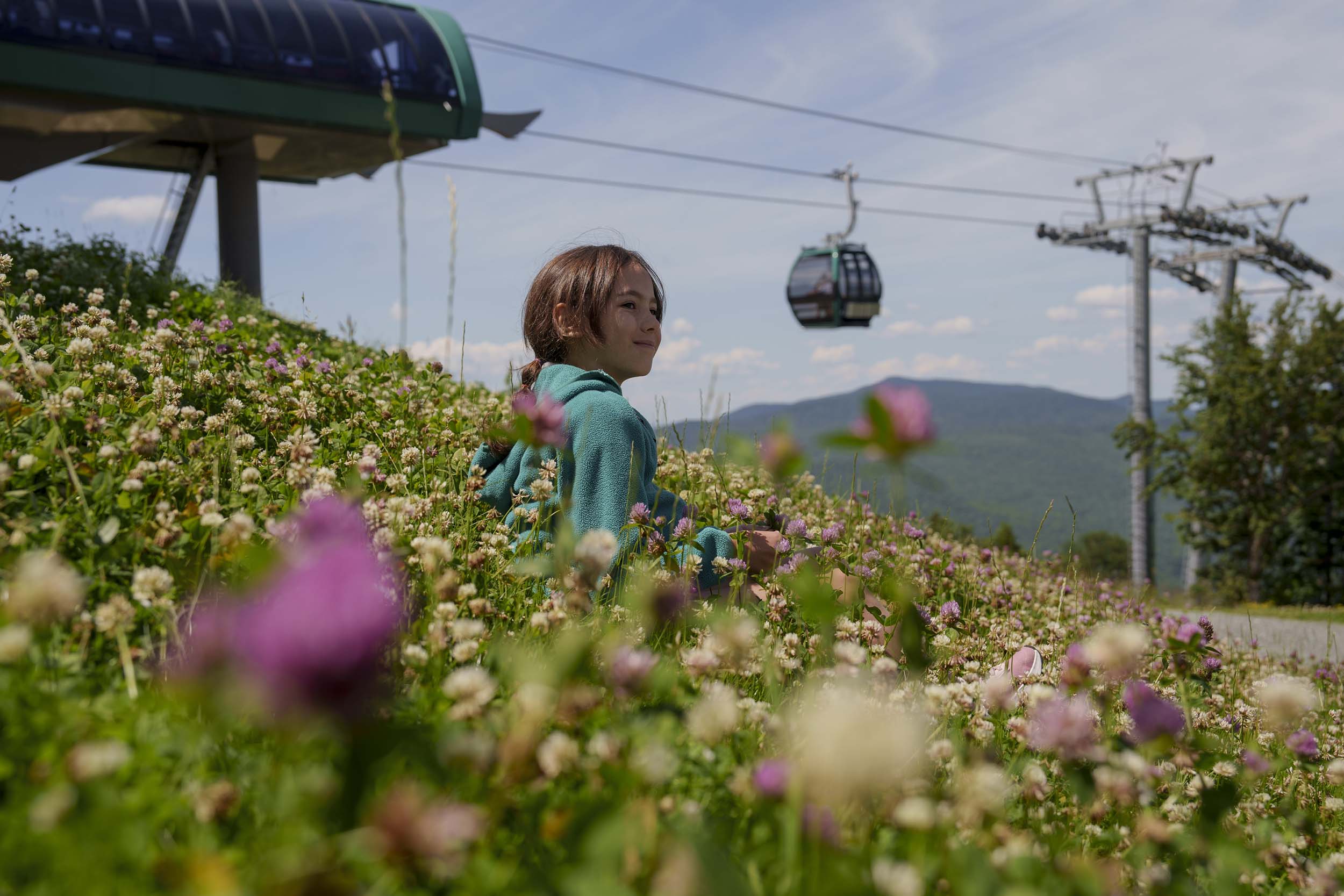 A girl walks through a flower meadow on Mount Washington with the gondola behind her.