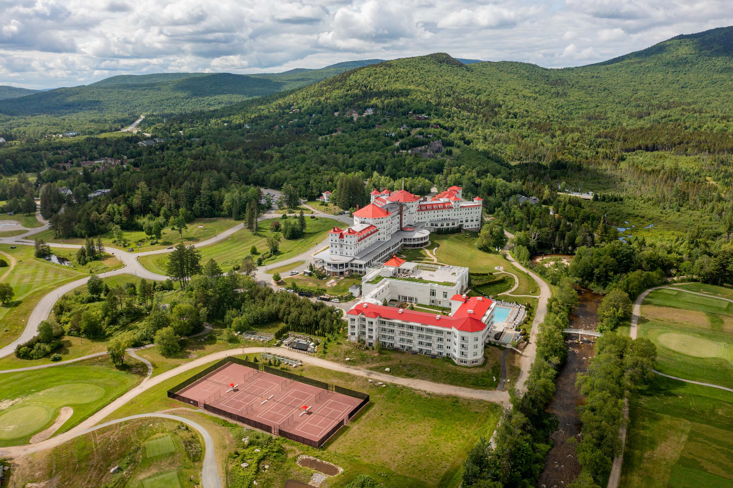 A wide aerial view of The OMNI Mount Washington Resort and Spa with the tennis courts in Summer