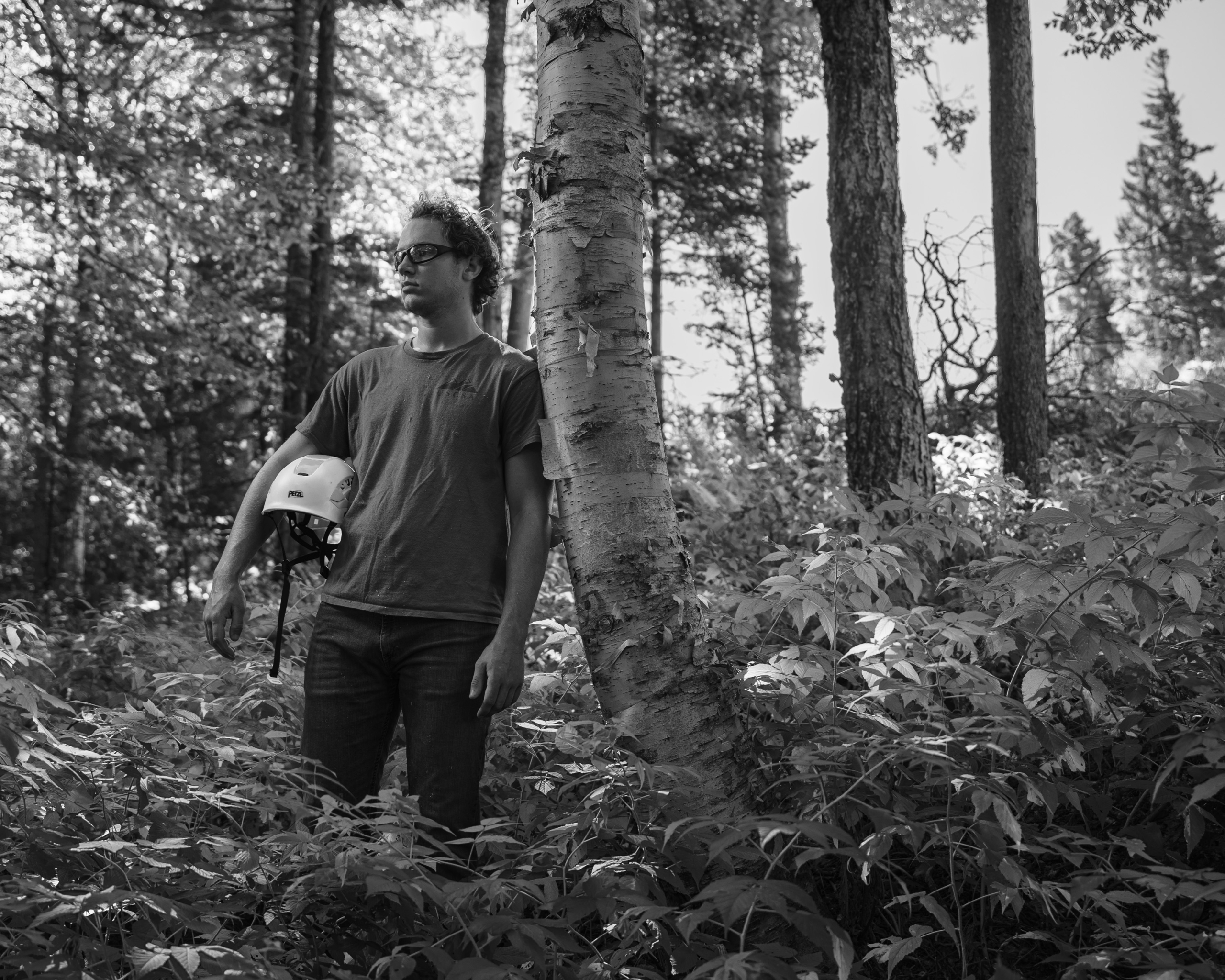 A person leaning against a tree holding a helmet at Bretton Woods