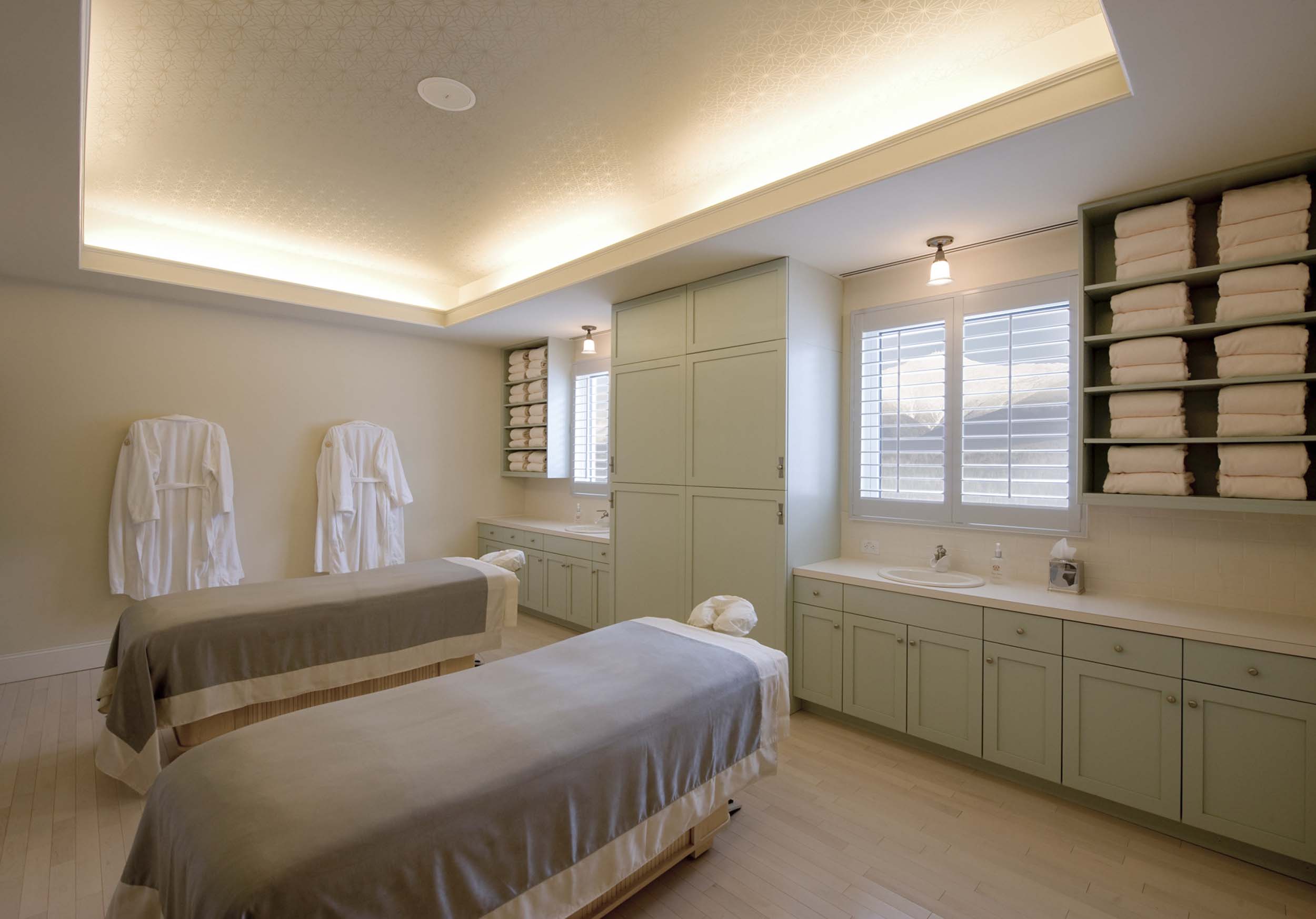 Elegant spa treatment room with two massage tables, soft lighting, and neatly stacked towels along the walls at Mount Washington Resort and Spa.