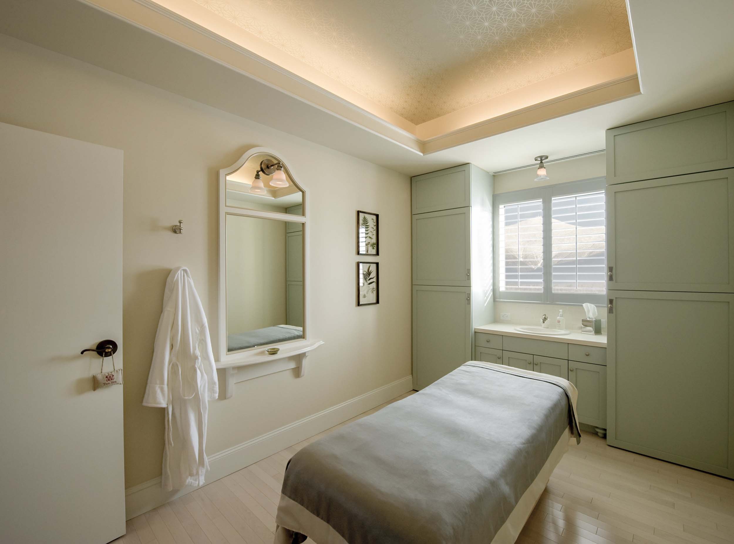 Elegant spa treatment room with a massage table, soft lighting, and a bath robe hung on the wall at Mount Washington Resort and Spa.