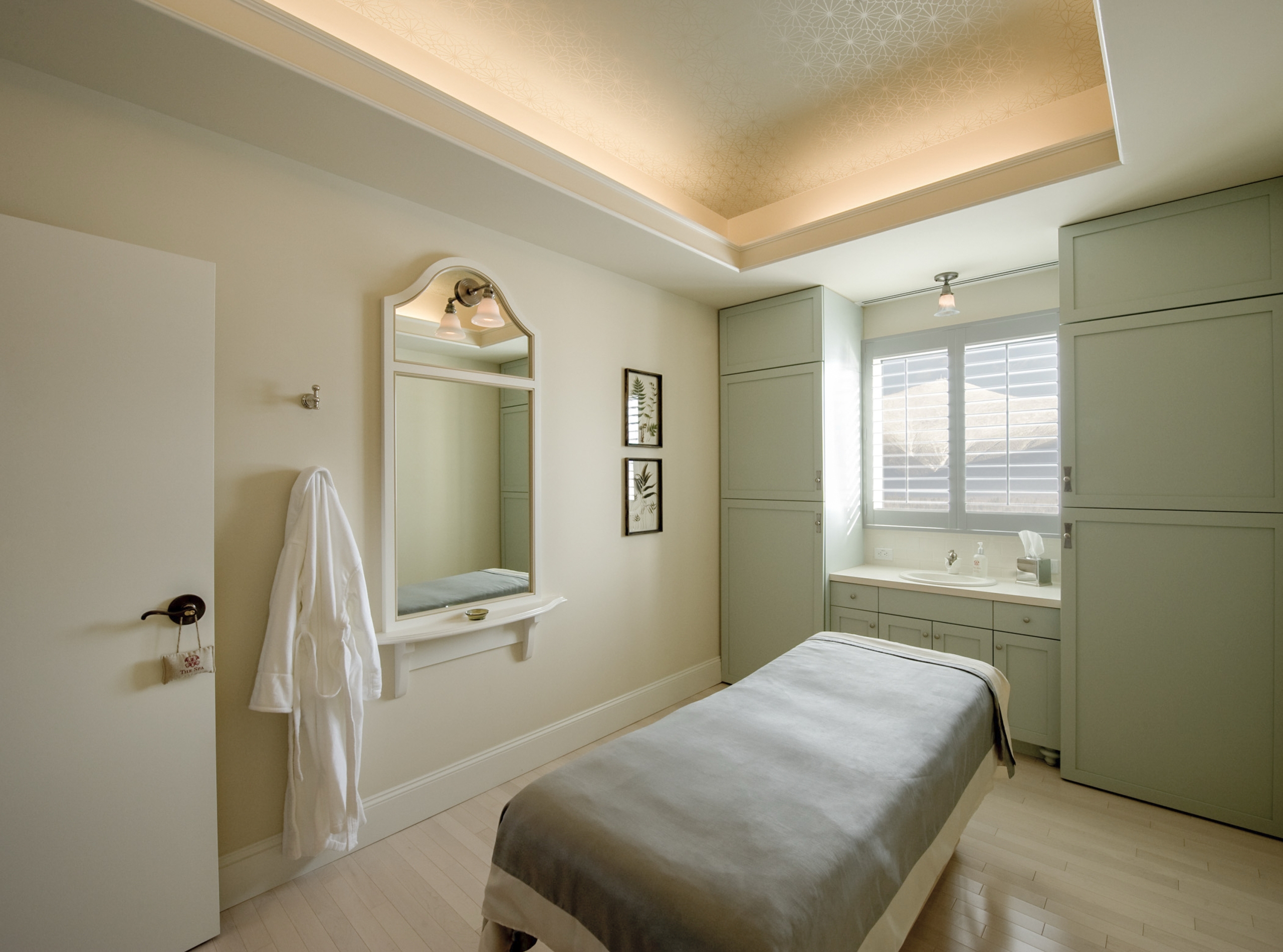 Elegant spa treatment room with a massage table, soft lighting, and a bath robe hung on the wall at Mount Washington Resort and Spa.