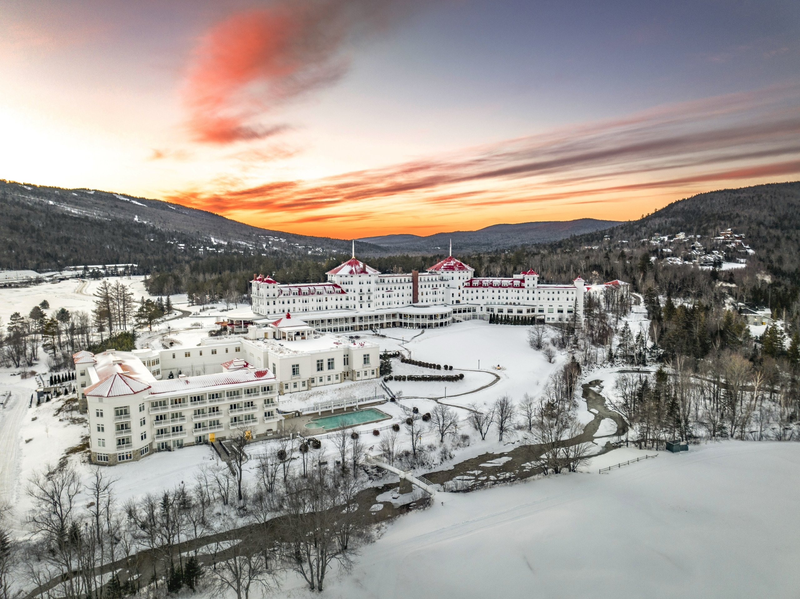 Mount Washington Resort and Spa sits at the base of snowy mountains glowing under a colorful sunset.