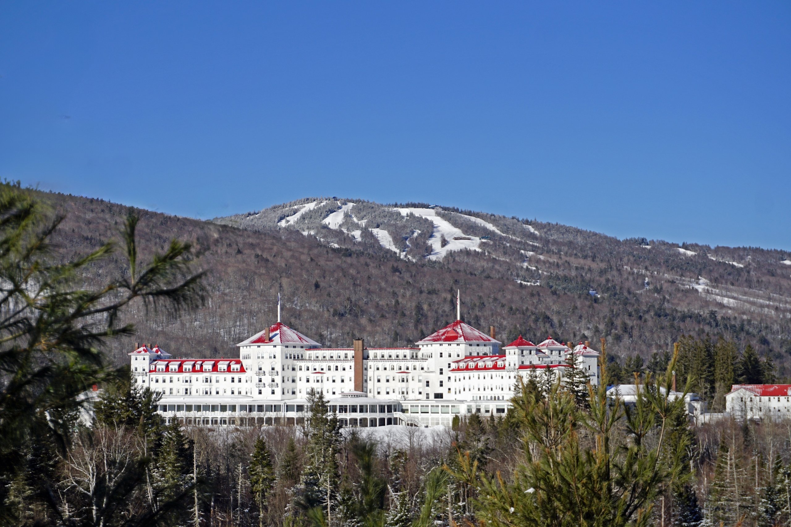 Mount Washington Resort and Spa is nestled in a wintry forest with a snow-covered mountain and ski trails rising behind it.