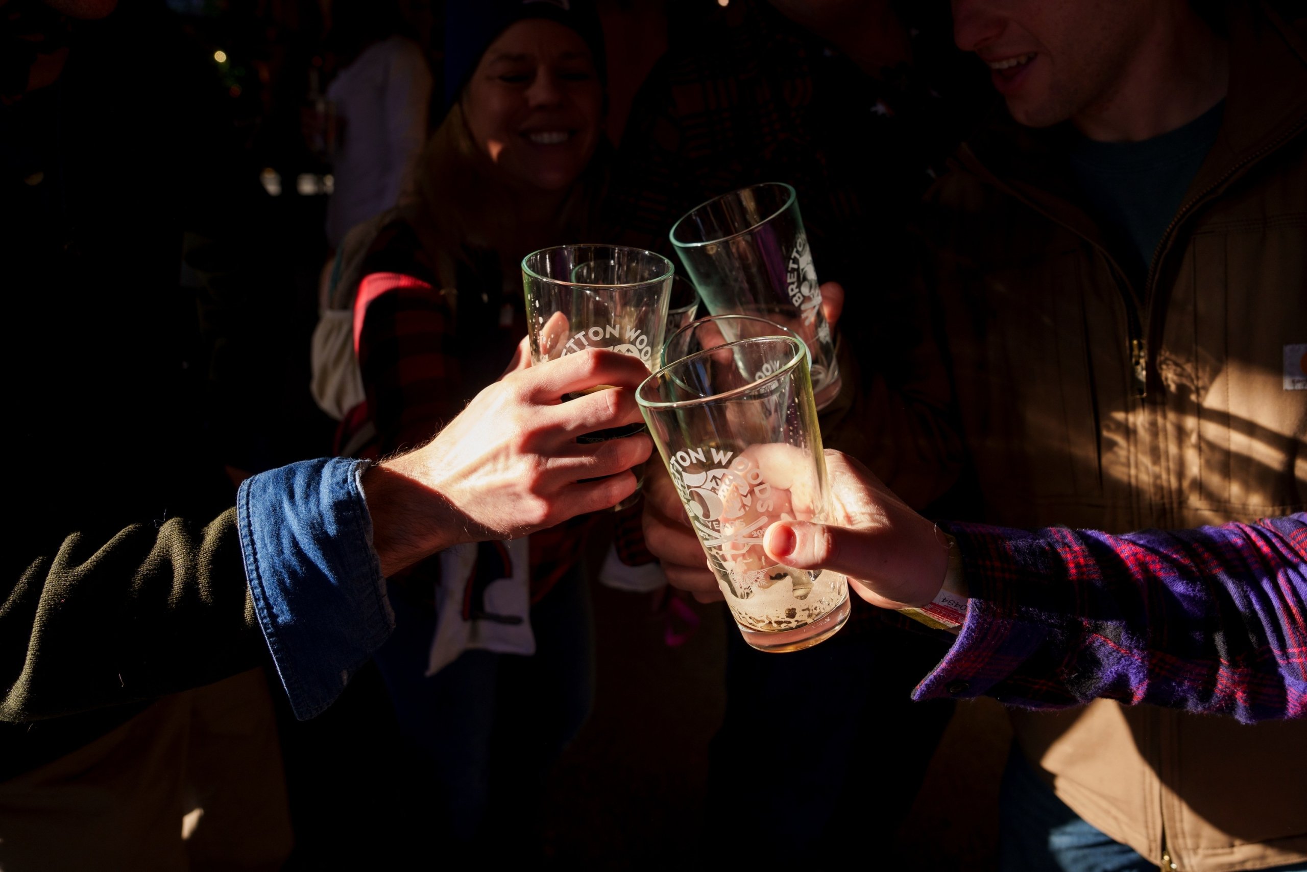 A close-up shot of four people's hands raising glasses for a celebratory toast. The clear glasses are branded 