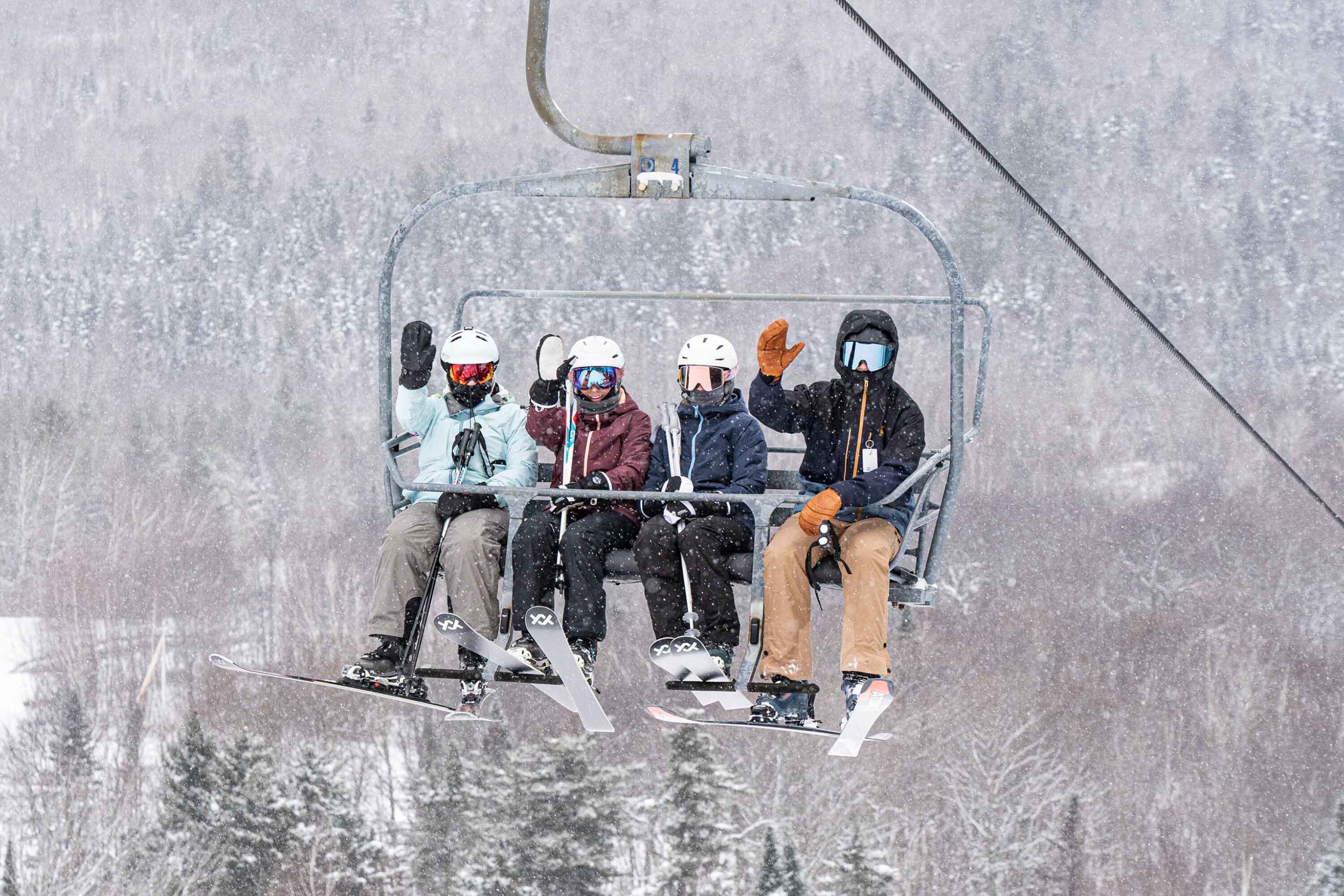 Four skiers wave while riding a ski lift up the snowy mountain at Bretton Woods.