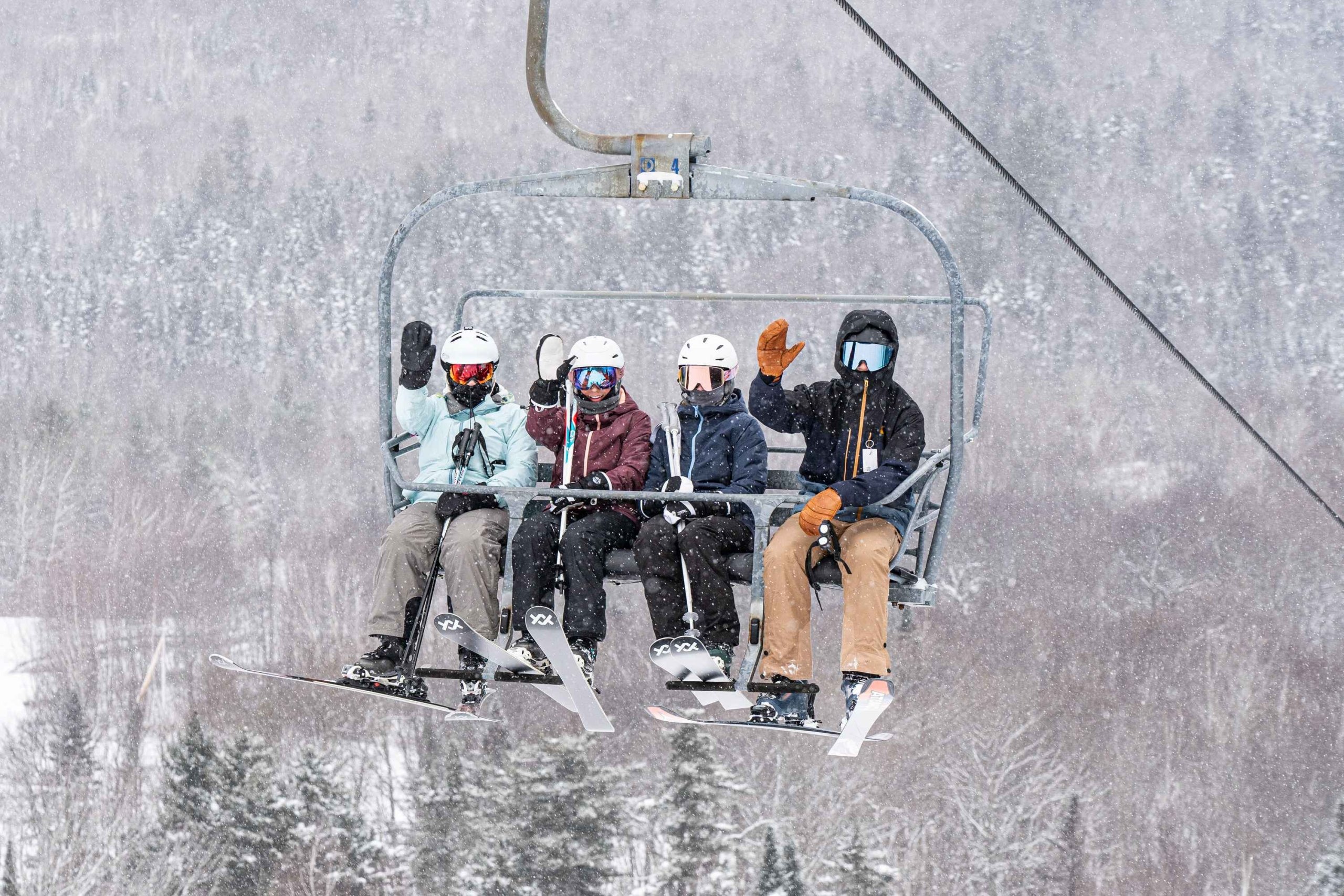 Four skiers wave while riding a ski lift up the snowy mountain at Bretton Woods.