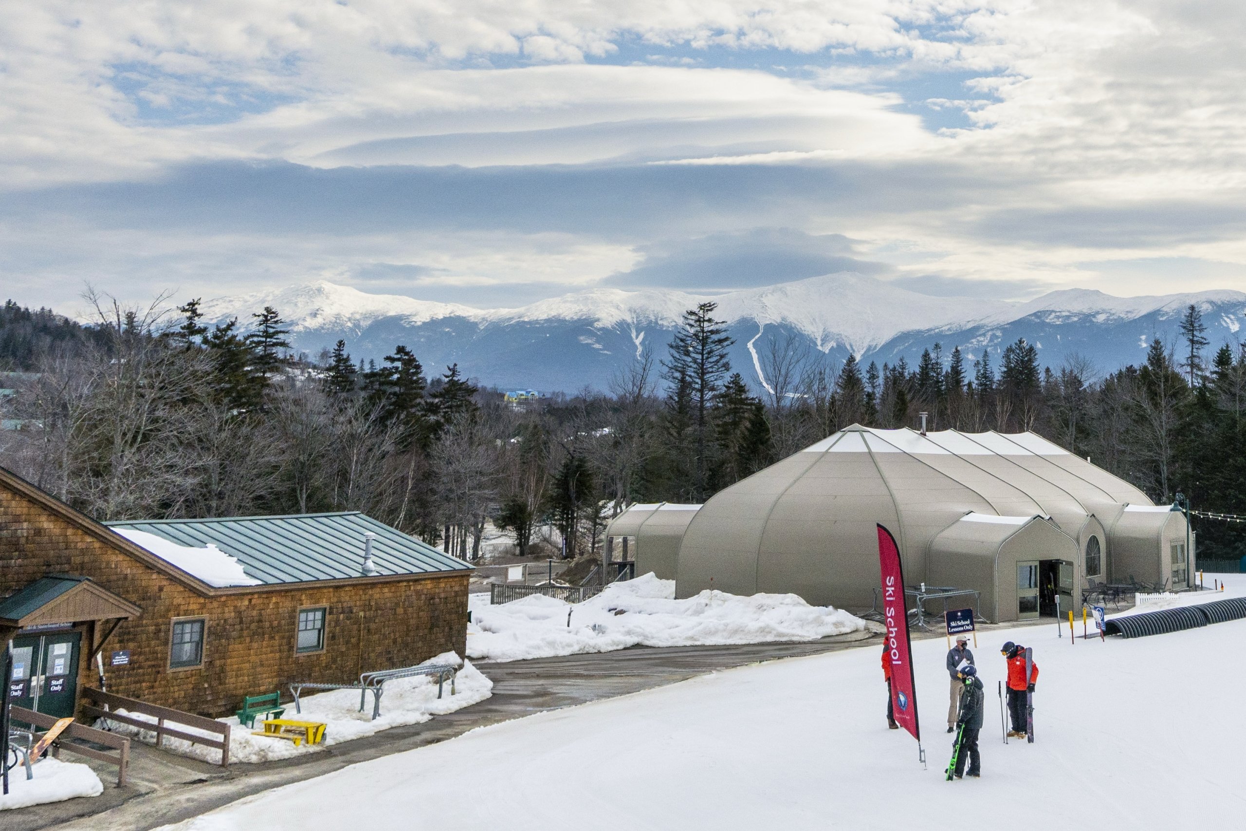 Skiers stand near a “Ski School” sign at Bretton Woods with snow-covered mountains in the background.