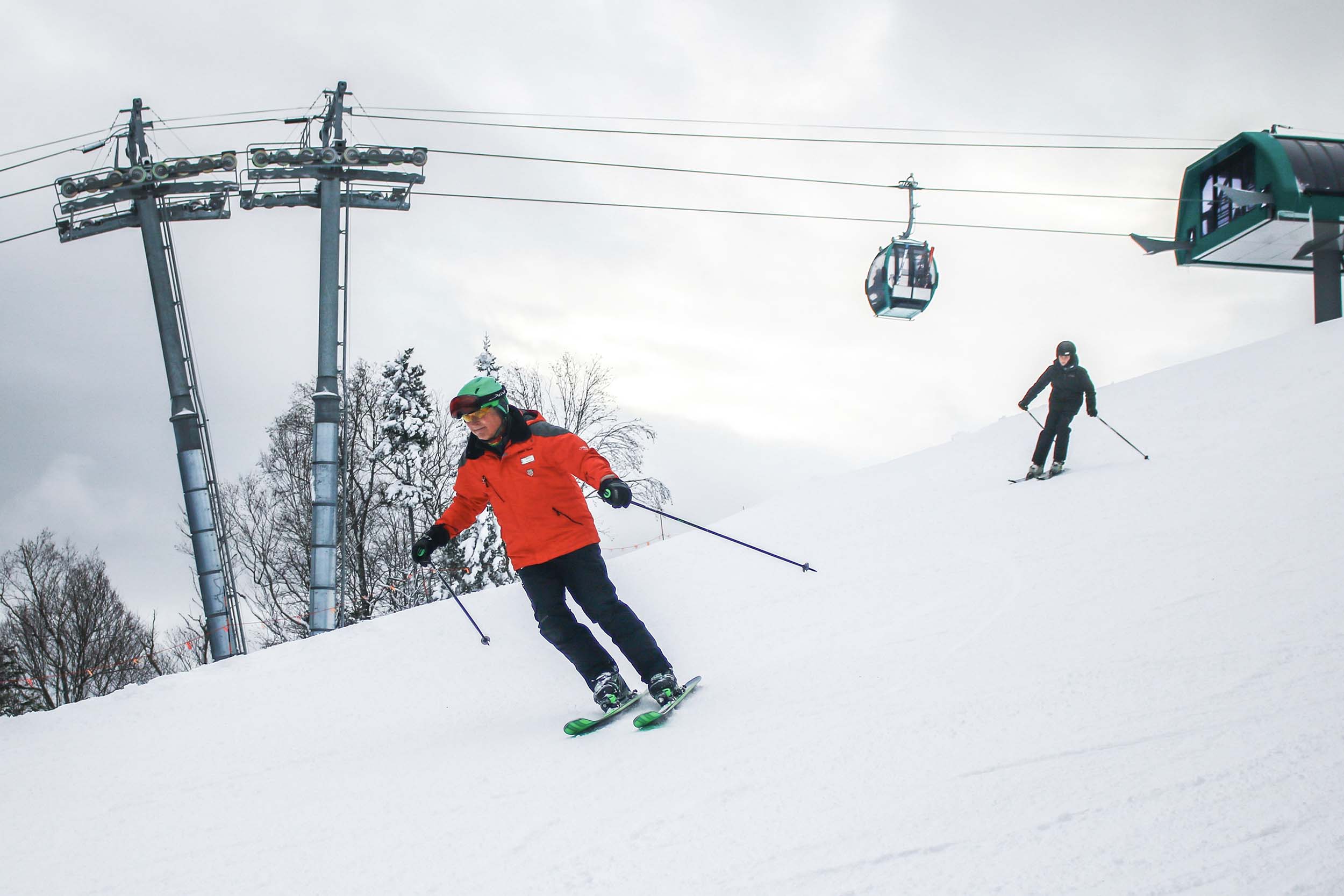 Two skiers descend the snowy mountain with the ski lift in the background at Bretton Woods.