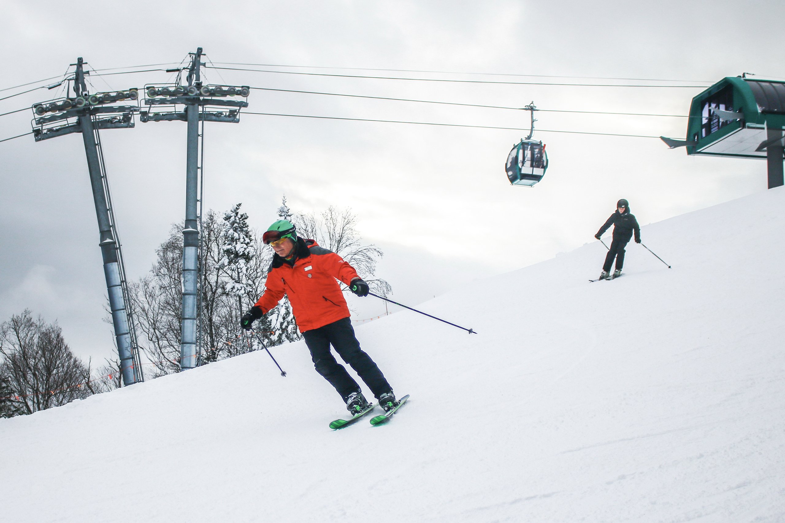 Two skiers descend the snowy mountain with the ski lift in the background at Bretton Woods.