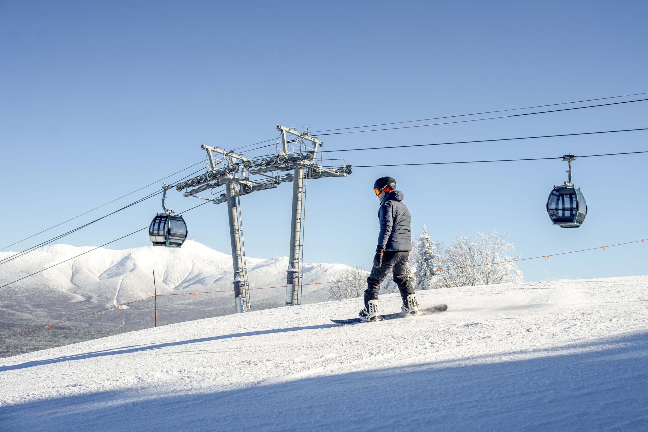 A snowboarder starts descending a run past the gondola at Bretton Woods.