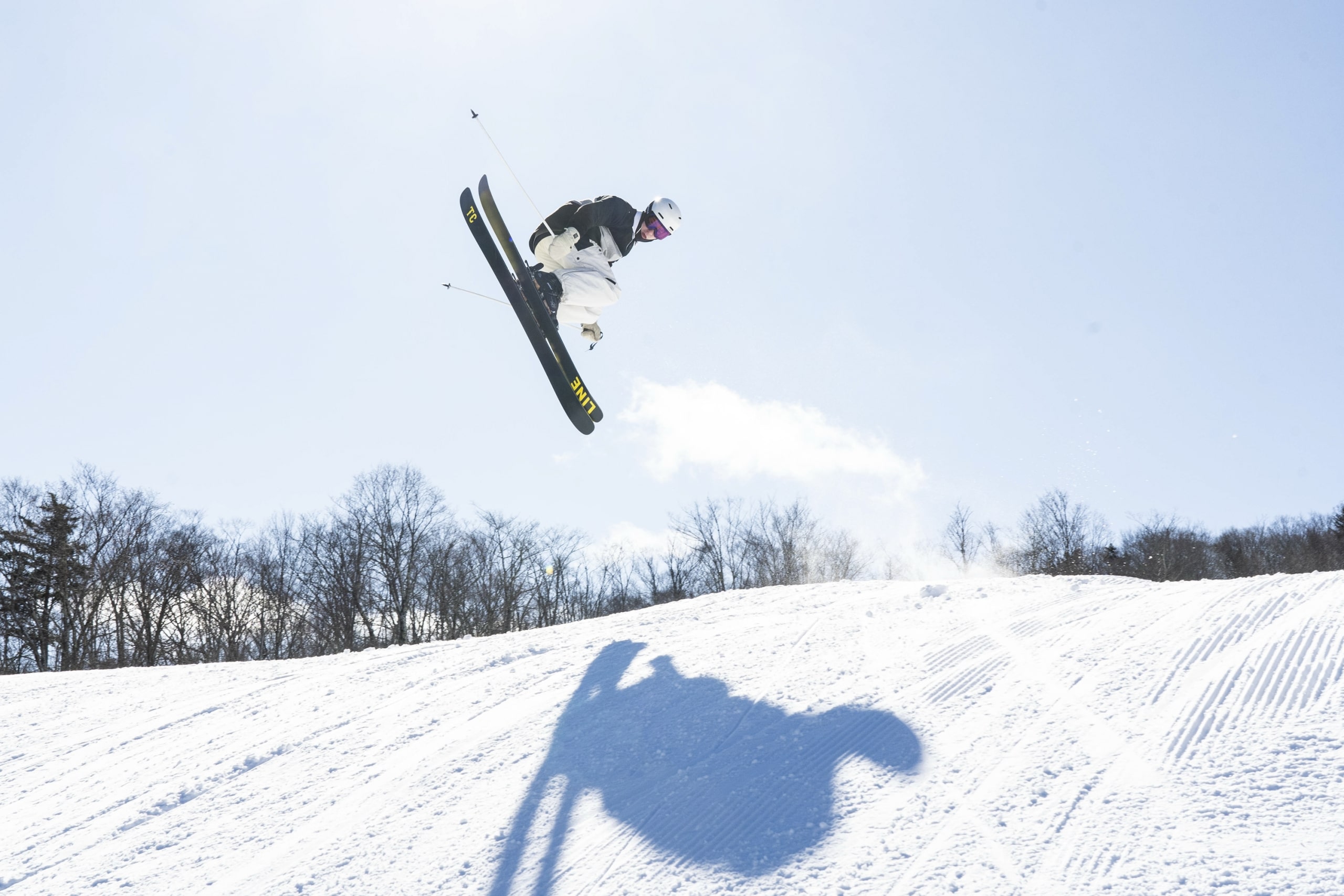 A skier performs a high ski jump through the air against a clear, sunny sky at Bretton Woods.