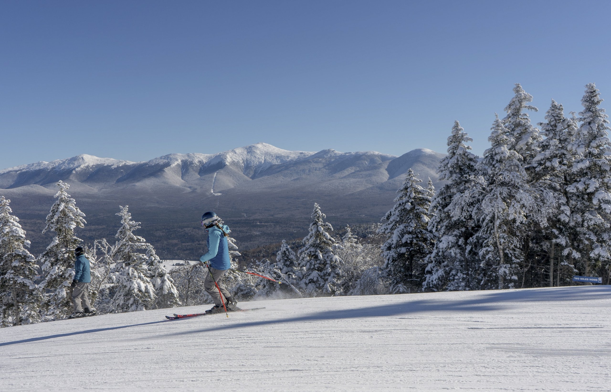 A skier glides down a snowy trail at Bretton Woods with a view of snow-covered mountains in the distance.
