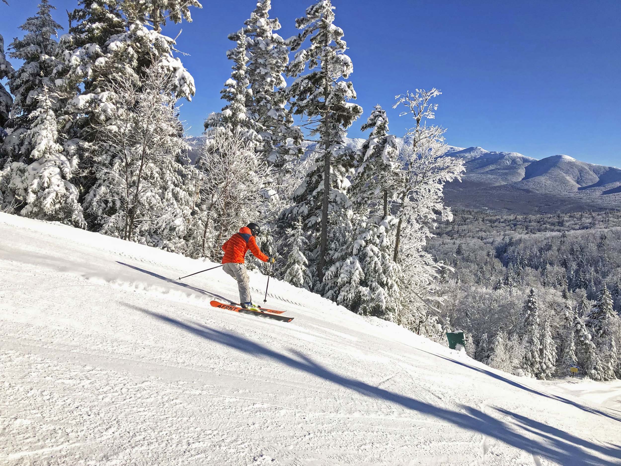 A skier glides down a snowy slope at Bretton Woods with a view of distant mountains.