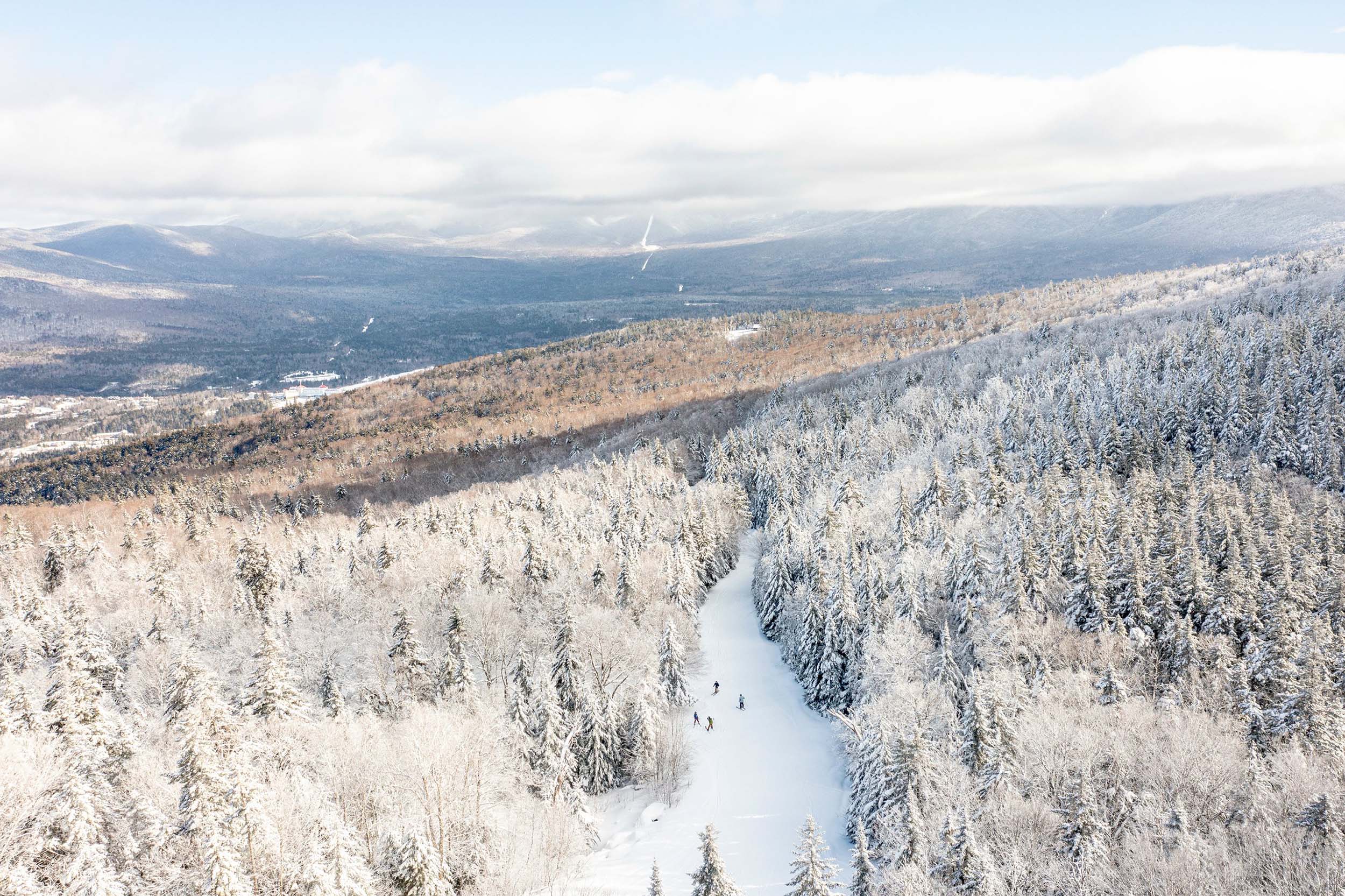 Aerial view of a ski trail amongst a forest of trees and snow-capped mountains at Bretton Woods.